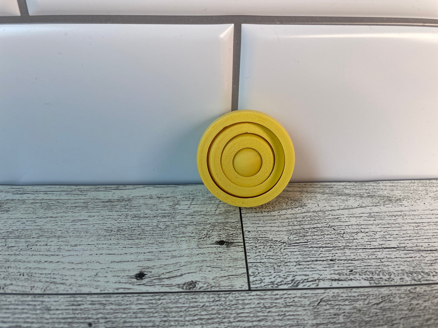 A yellow gyro fidget without keychain on a light wood grain and white tile background.