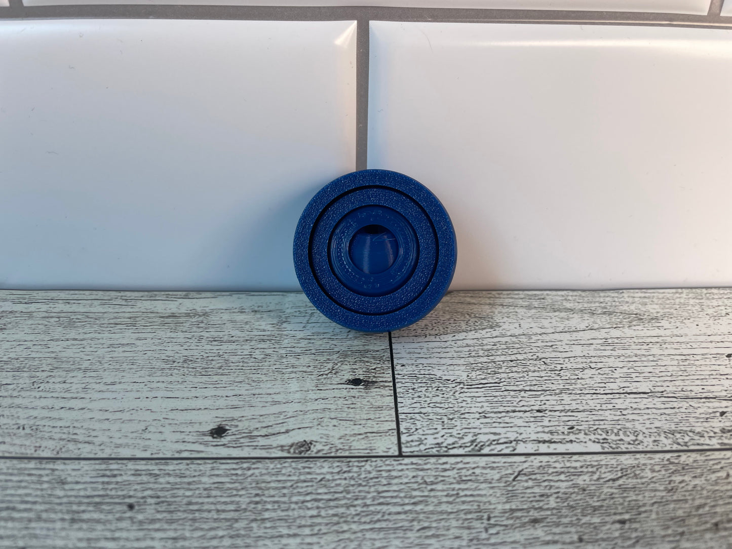 A blue gyro fidget without keychain on a light wood grain and white tile background.