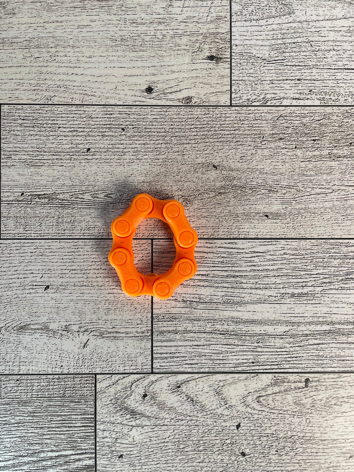 A orange chain link on a wood backdrop. The chain is arranged in a oval shape and there are four links