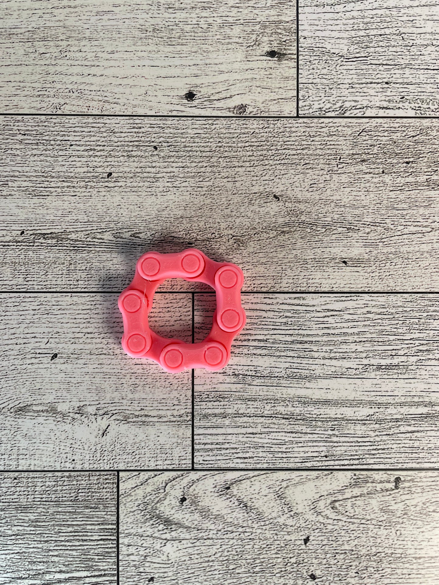 A pink chain link on a wood backdrop. The chain is arranged in a circle shape and there are four links