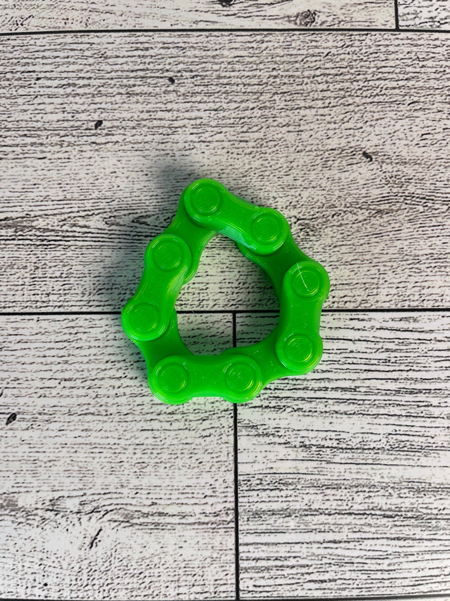 A lime green chain link on a wood backdrop. The chain is arranged in a circle shape and there are four links