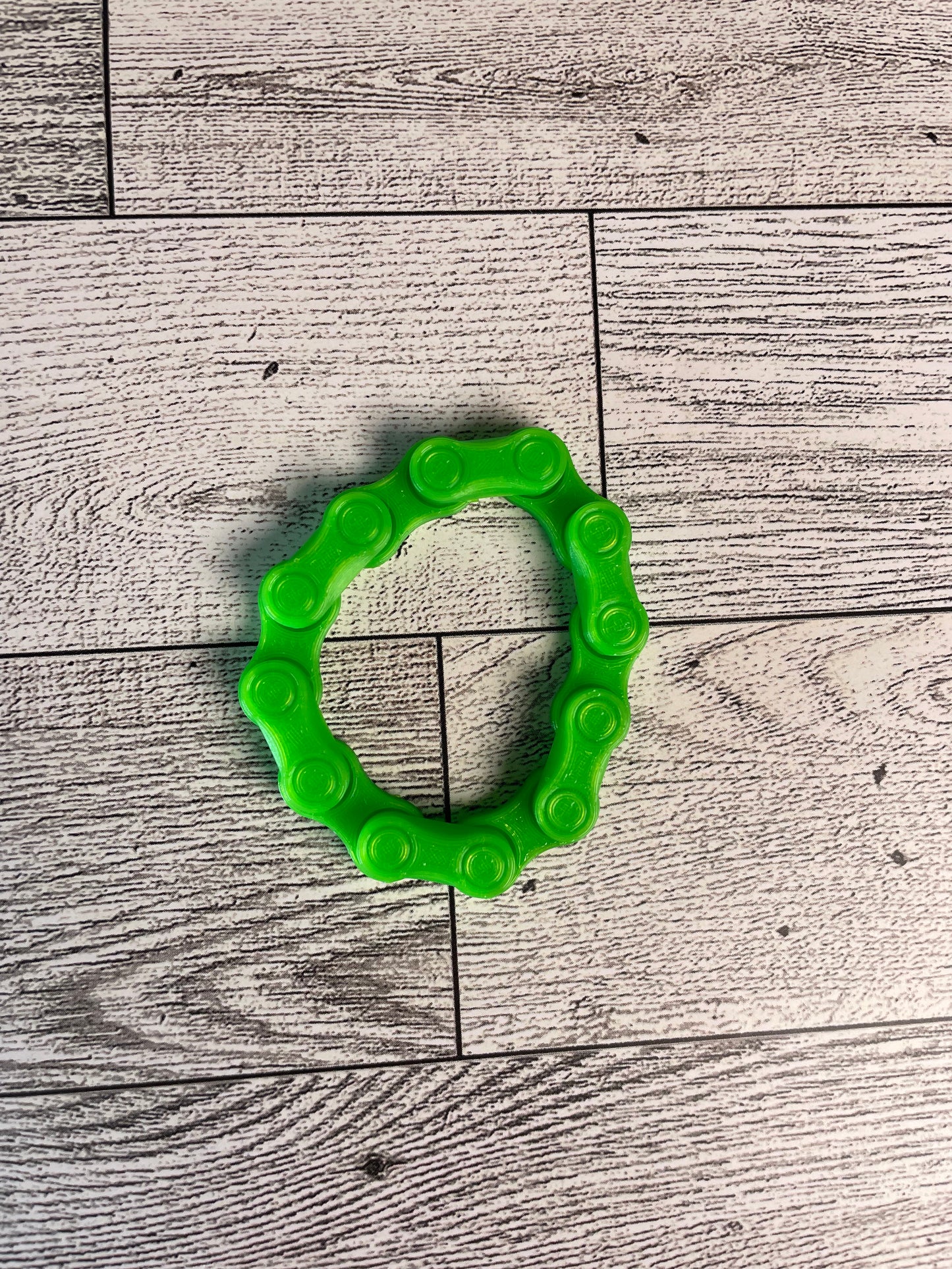 A lime green chain link on a wood backdrop. The chain is arranged in a circle shape and there are six links.