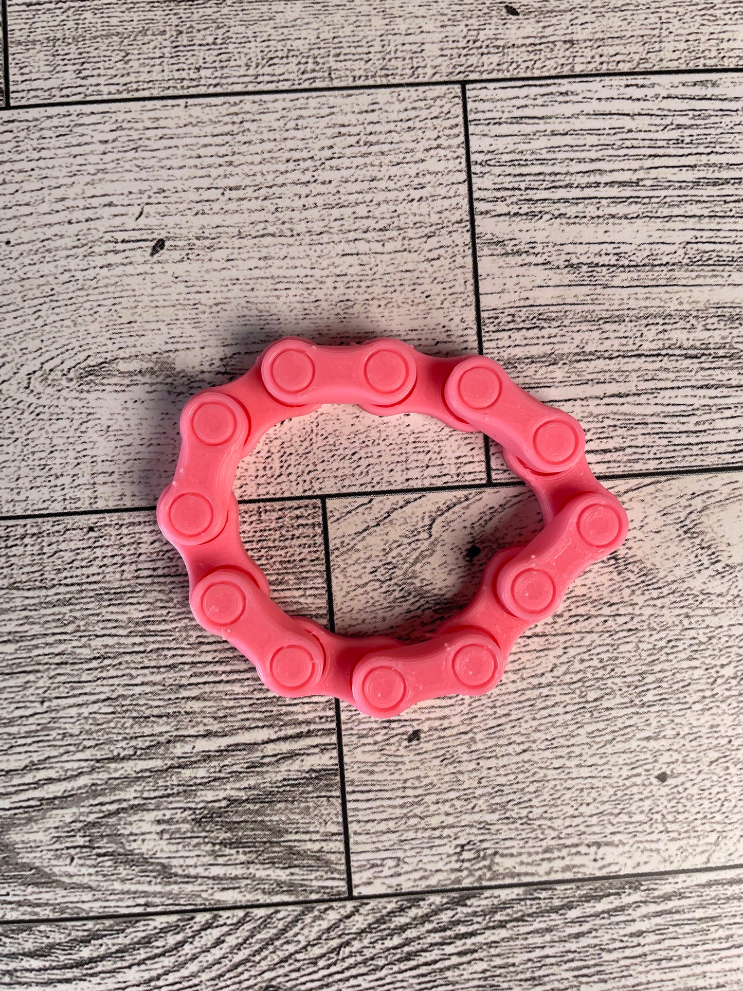 A pink chain link on a wood backdrop. The chain is arranged in a circle shape and there are six links.