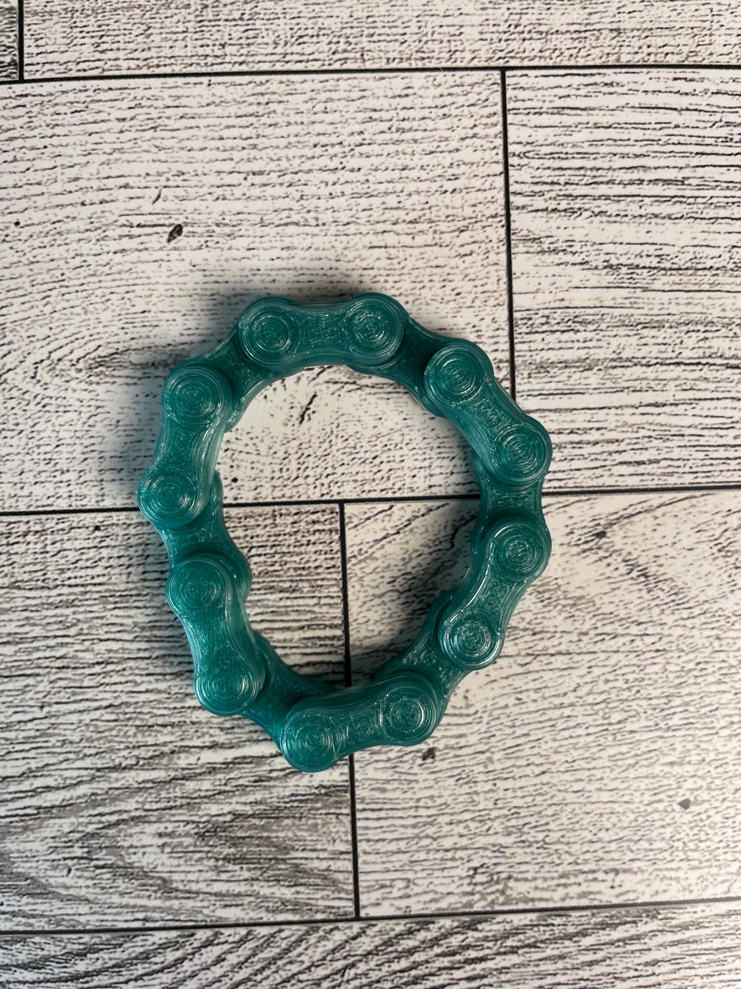 A translucent green chain link on a wood backdrop. The chain is arranged in a circle shape and there are six links.