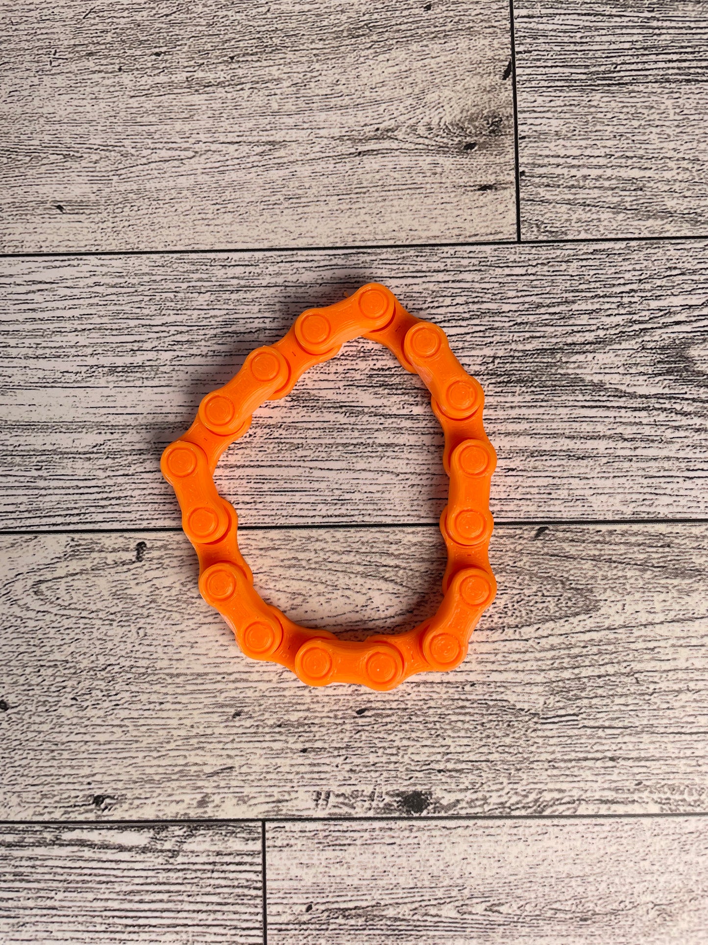 A orange chain link on a wood backdrop. The chain is arranged in a circle shape and there are eight links.
