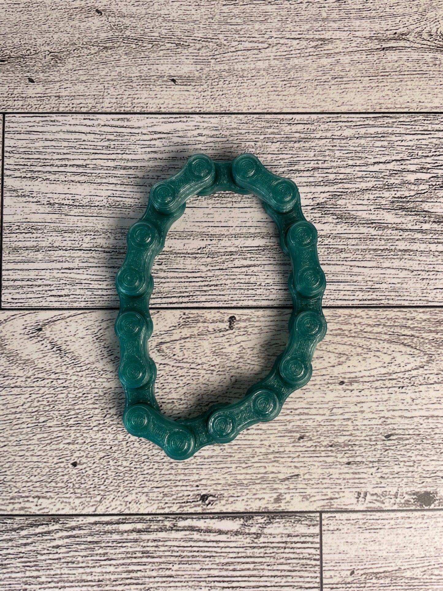 A translucent green chain link on a wood backdrop. The chain is arranged in a oval shape and there are eight links.