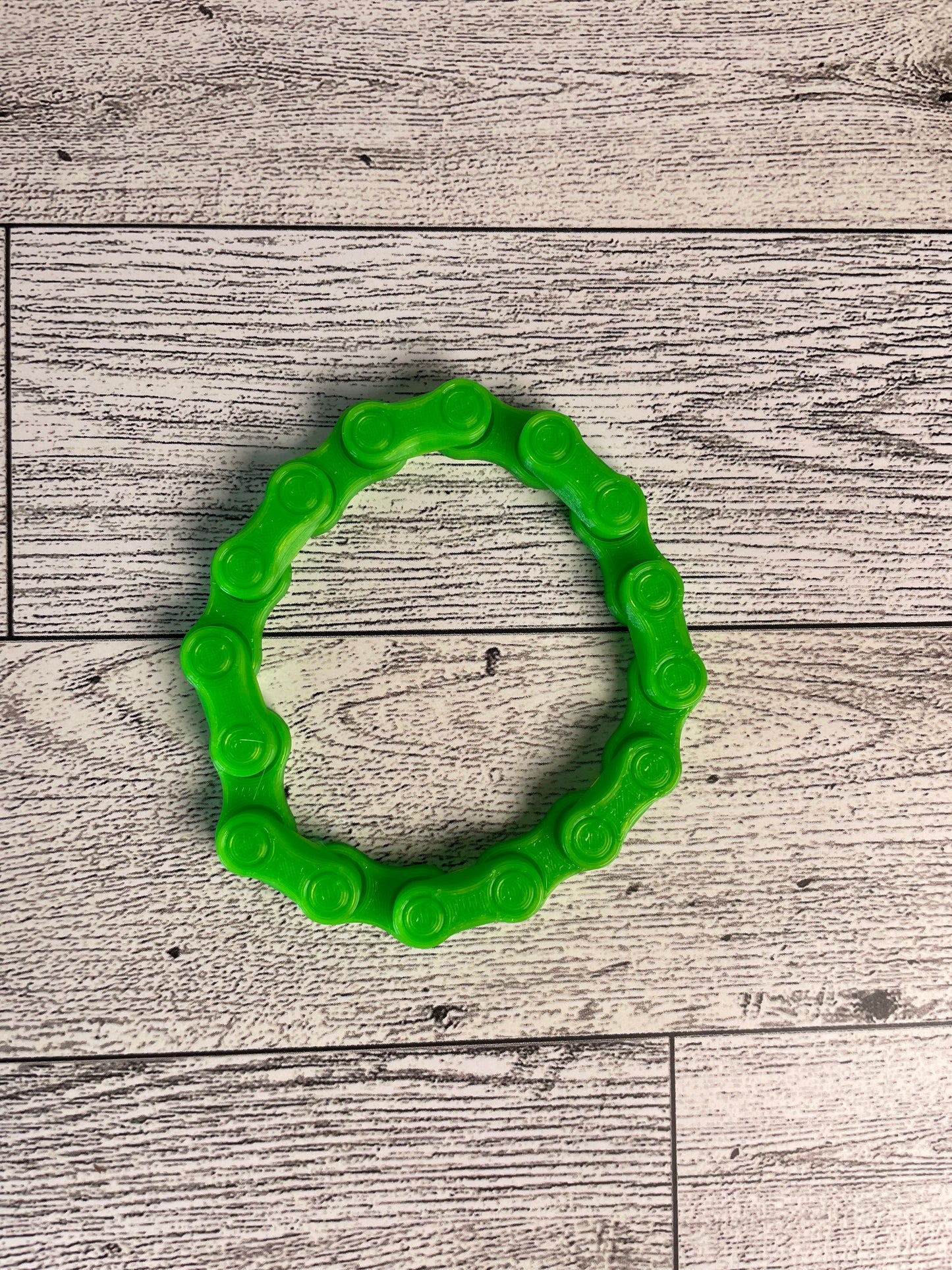 A lime green chain link on a wood backdrop. The chain is arranged in a circle shape and there are eight links.