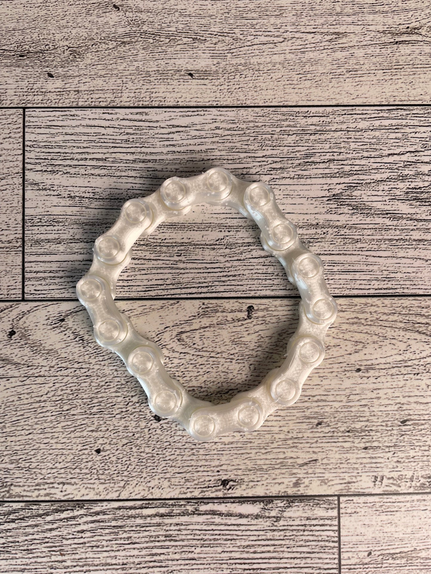 A shiny white chain link on a wood backdrop. The chain is arranged in a circle shape and there are eight links.