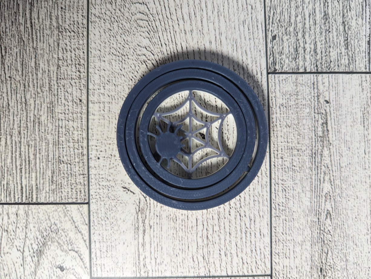 A white and grey Spider spinner laying flat on a light woodgrain