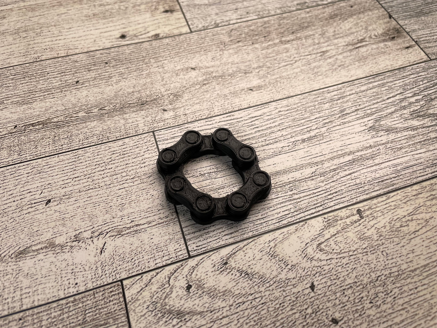 A black chain link on a wood backdrop. The chain is arranged in a circle and there are four links.