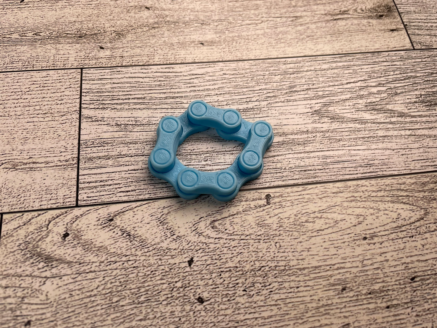 A light blue chain link on a wood backdrop. The chain is arranged in a squished circle and there are four links.