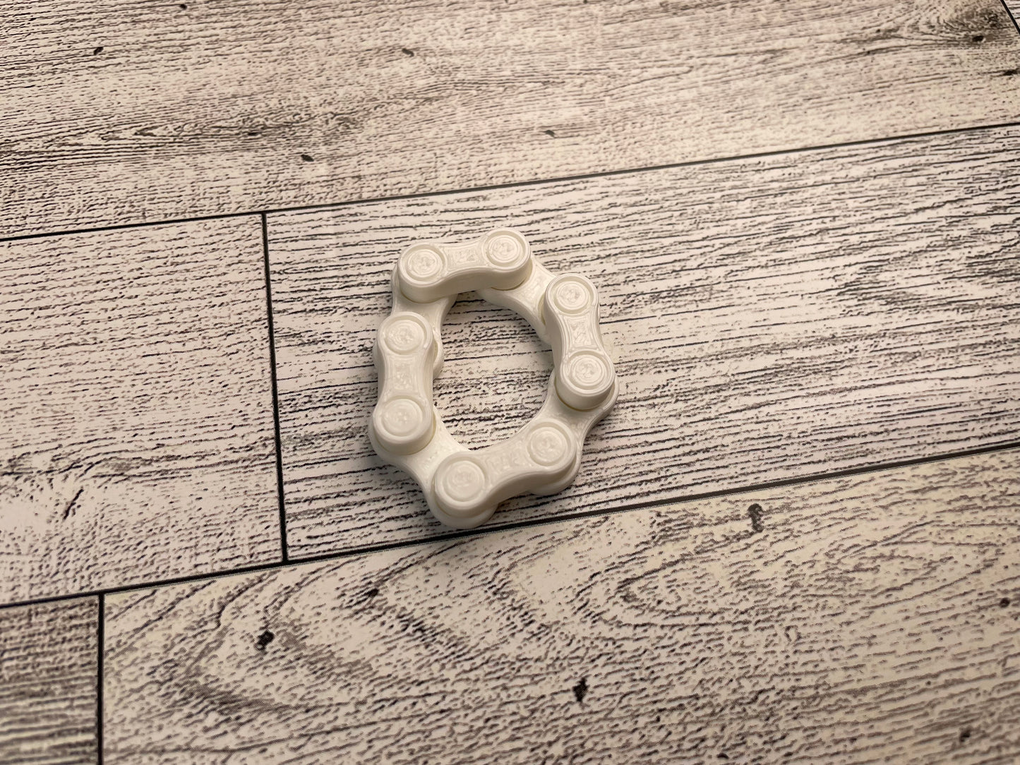 A white chain link on a wood backdrop. The chain is arranged in a squished circle and there are four links.