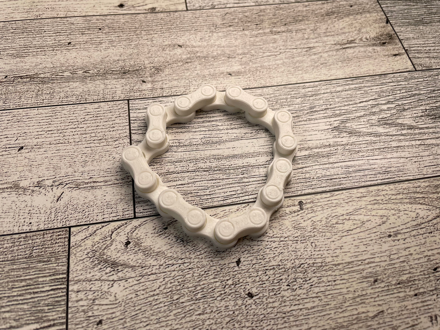 A white chain link on a wood backdrop. The chain is arranged in a squished circle and there are eight links.