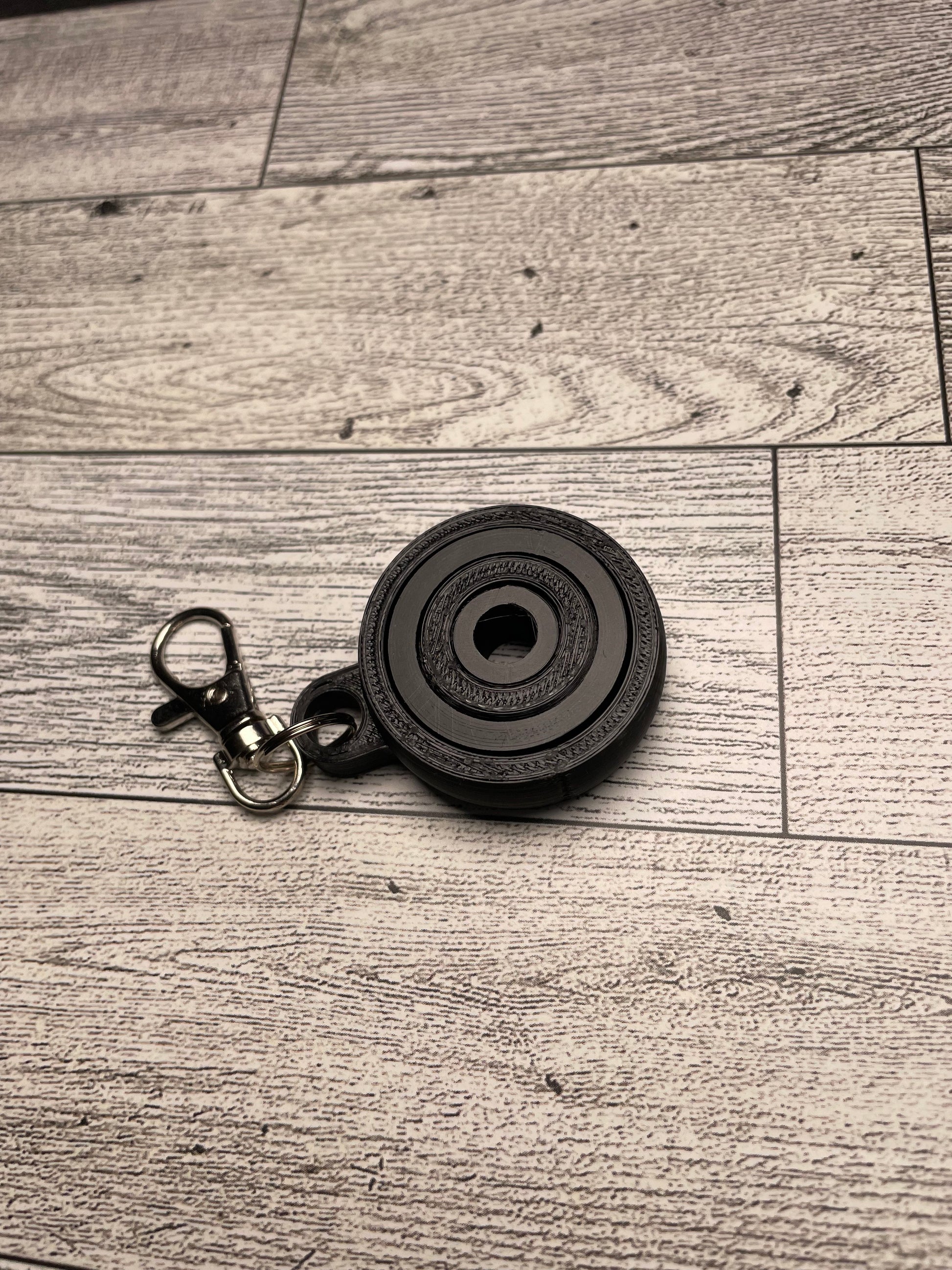 A black gyro fidget with keychain on a light wood grain background.