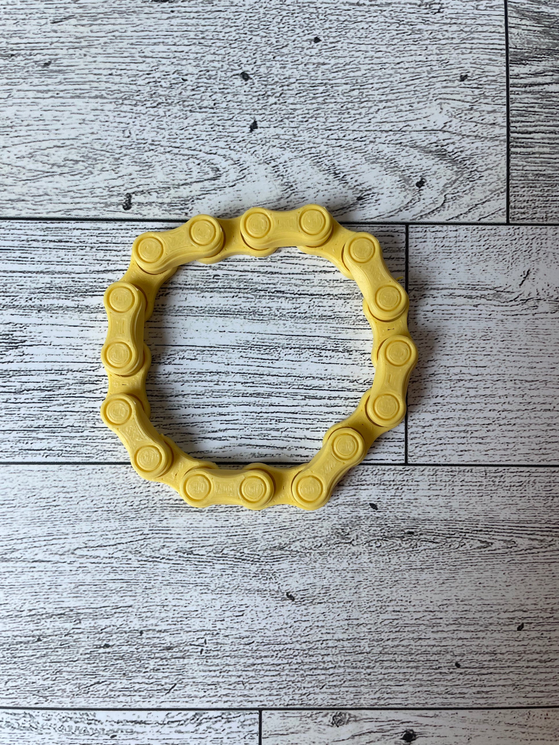 A yellow chain link on a wood backdrop. The chain is arranged in a circle shape and there are eight links.