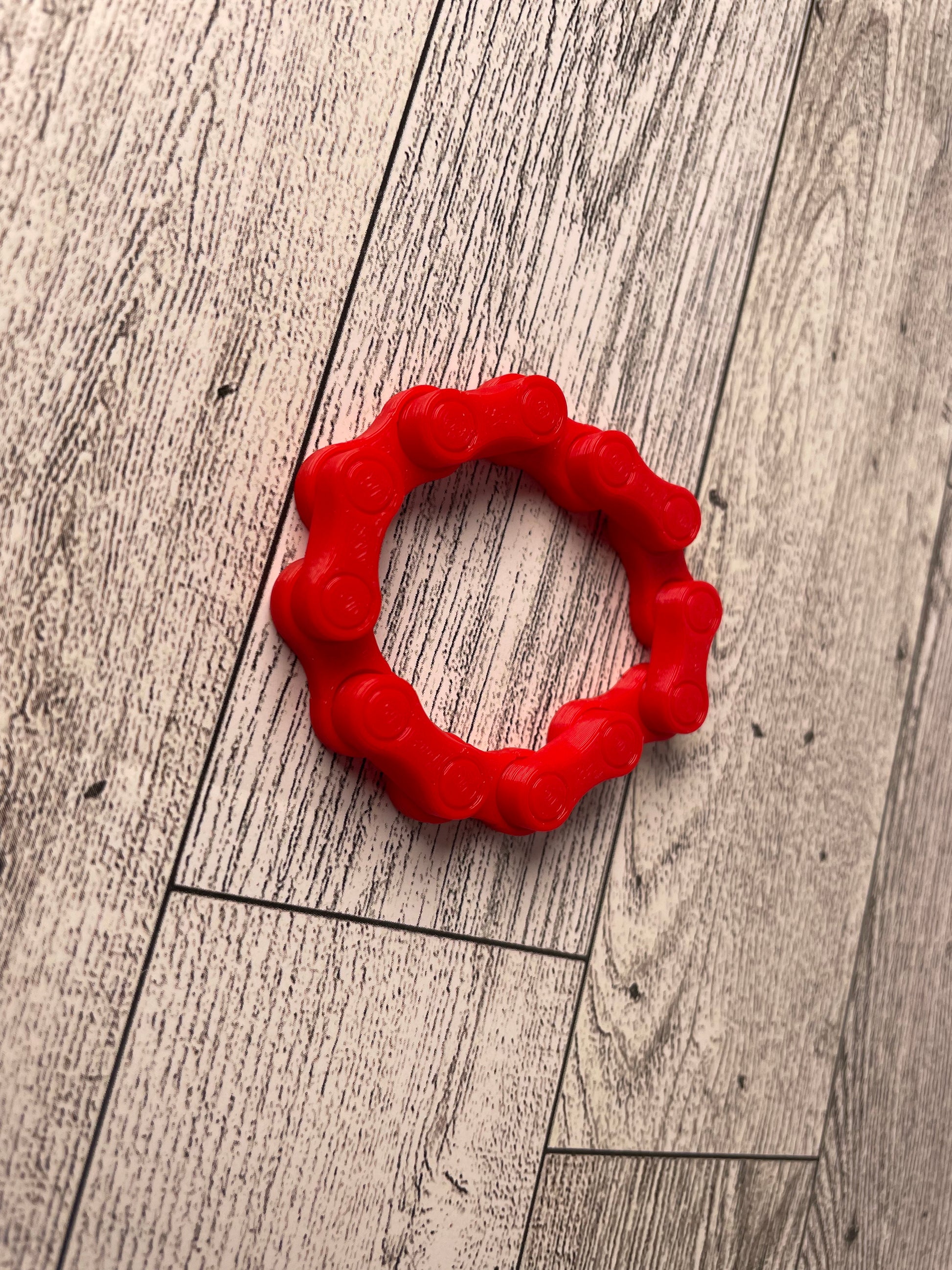 A red chain link on a wood backdrop. The chain is arranged in a circle shape and there are six links.