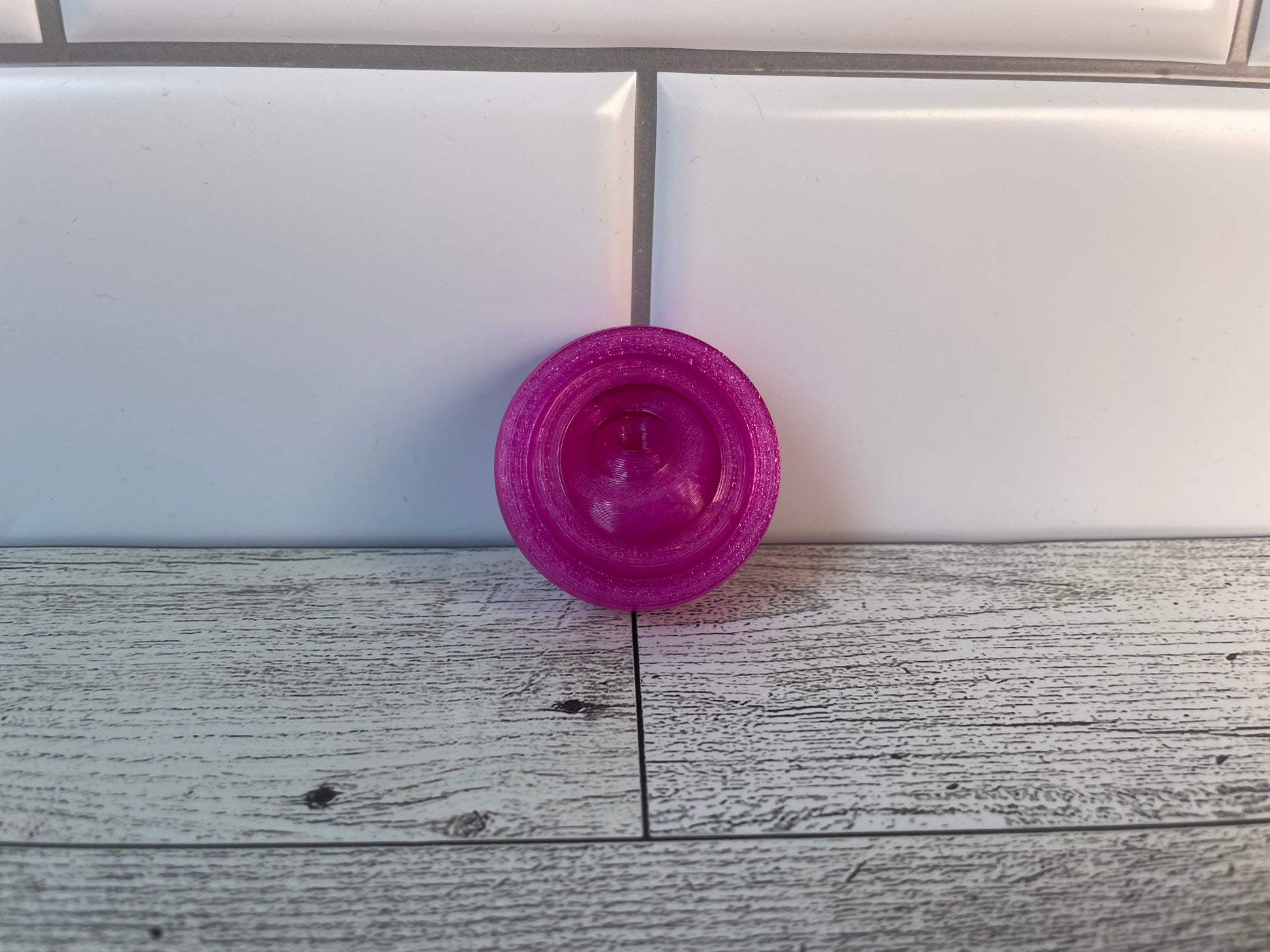 A translucent purple gyro fidget without keychain on a light wood grain and white tile background.