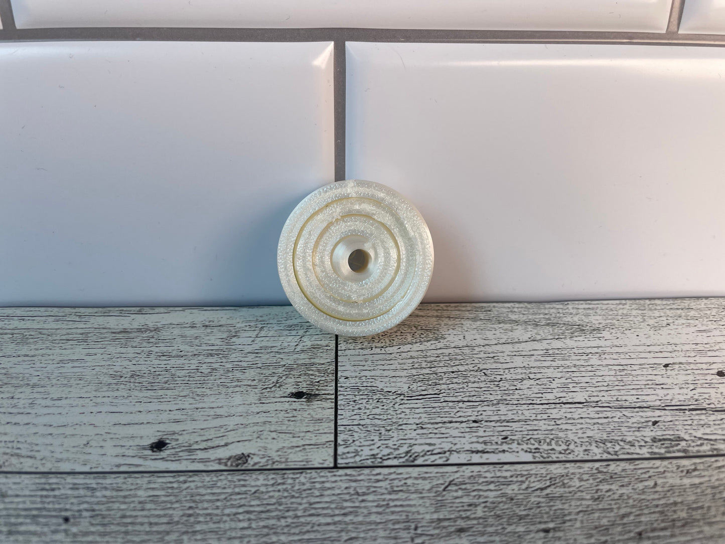 A shiny white gyro fidget without keychain on a light wood grain and white tile background.