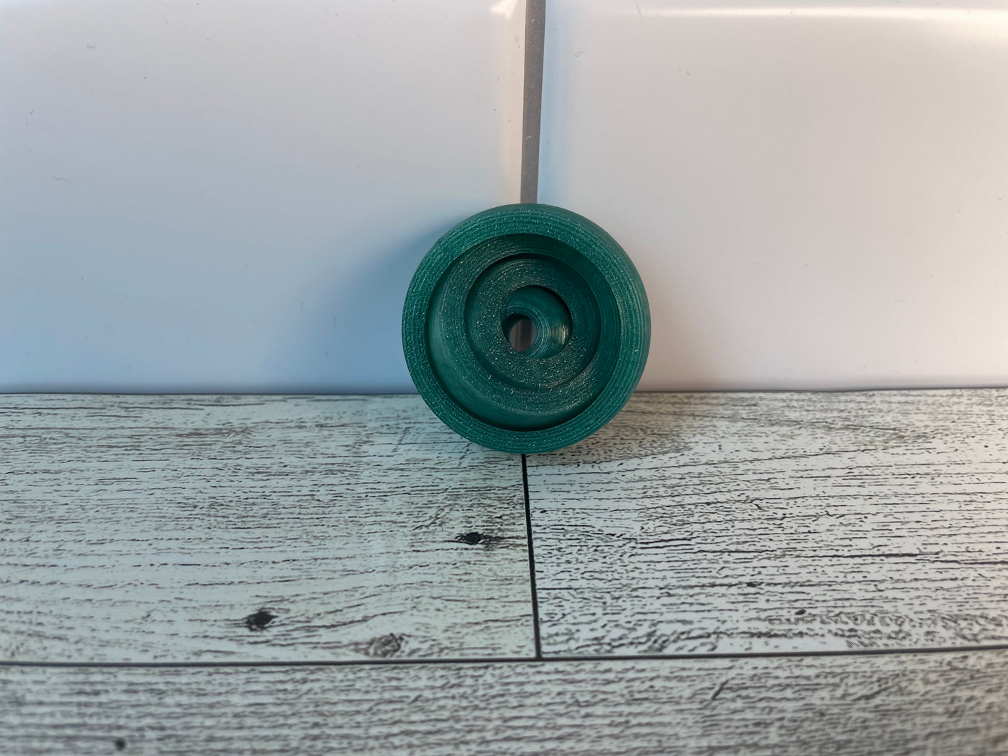 A translucent green gyro fidget without keychain on a light wood grain and white tile background.
