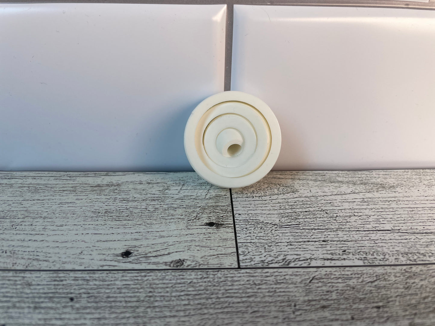 A white gyro fidget without keychain on a light wood grain and white tile background.