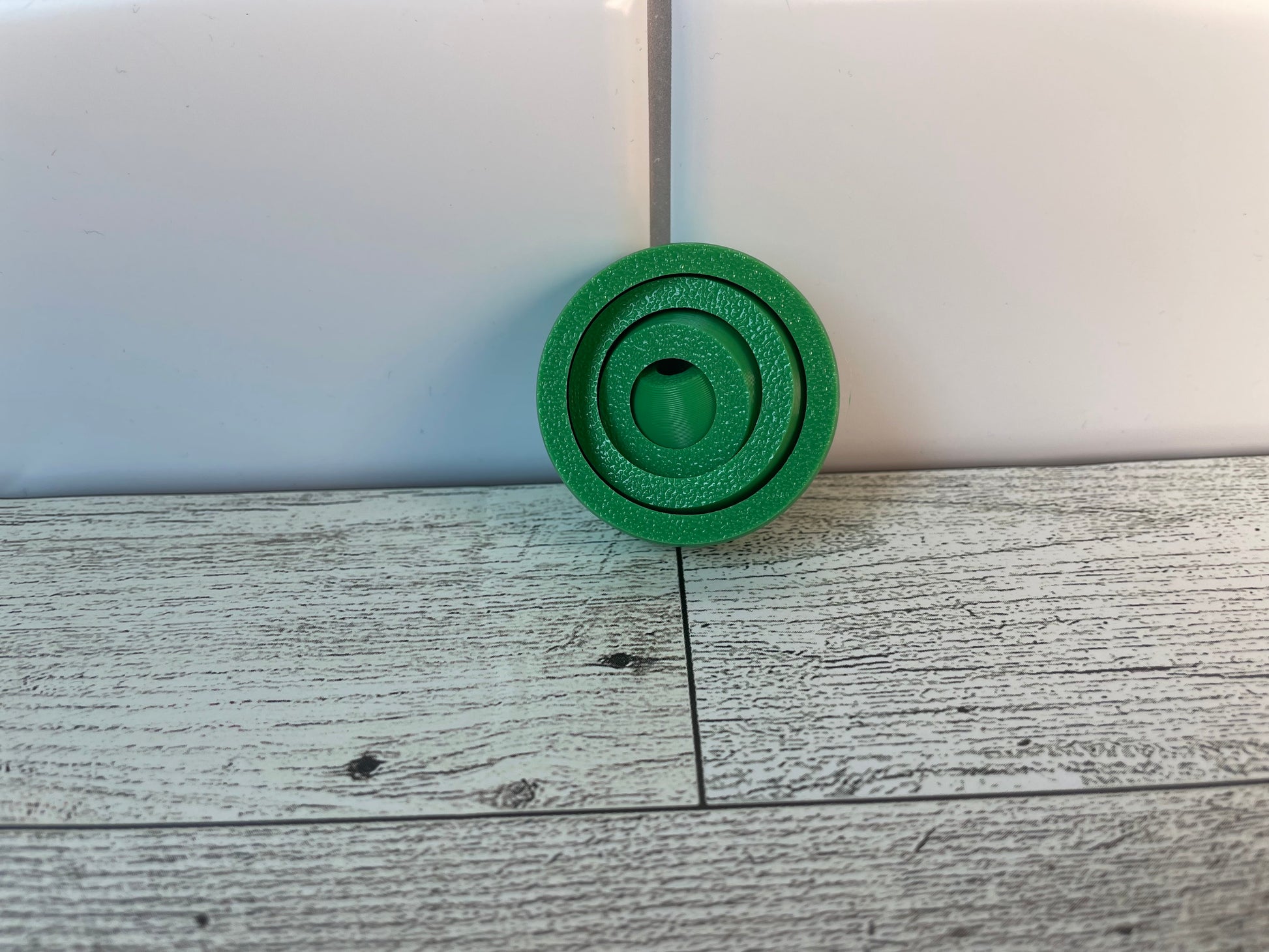 A green gyro fidget without keychain on a light wood grain and white tile background.