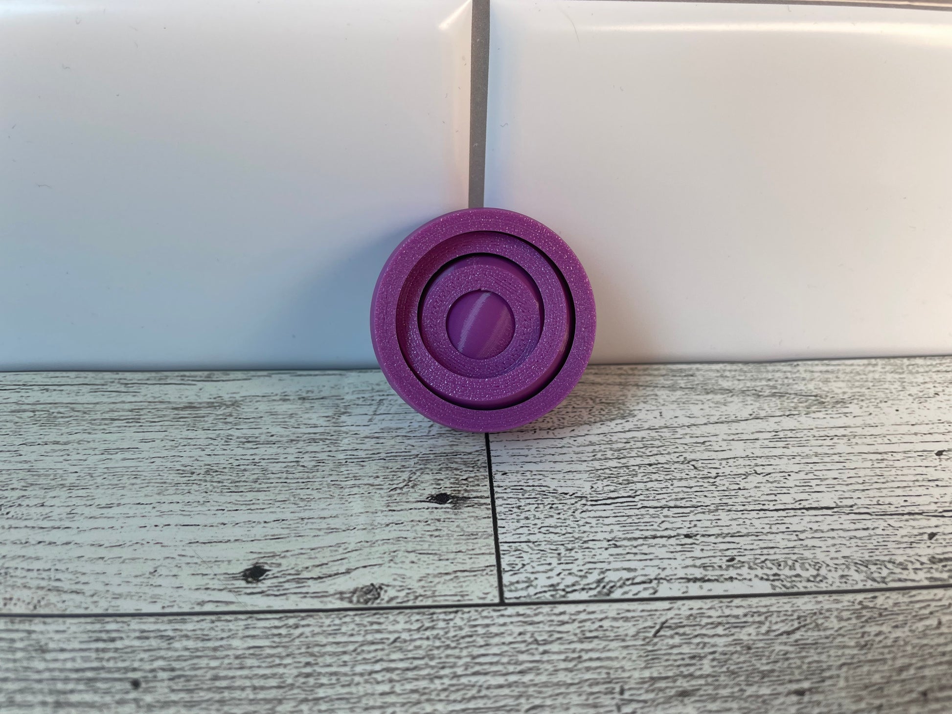 A purple gyro fidget without keychain on a light wood grain and white tile background.