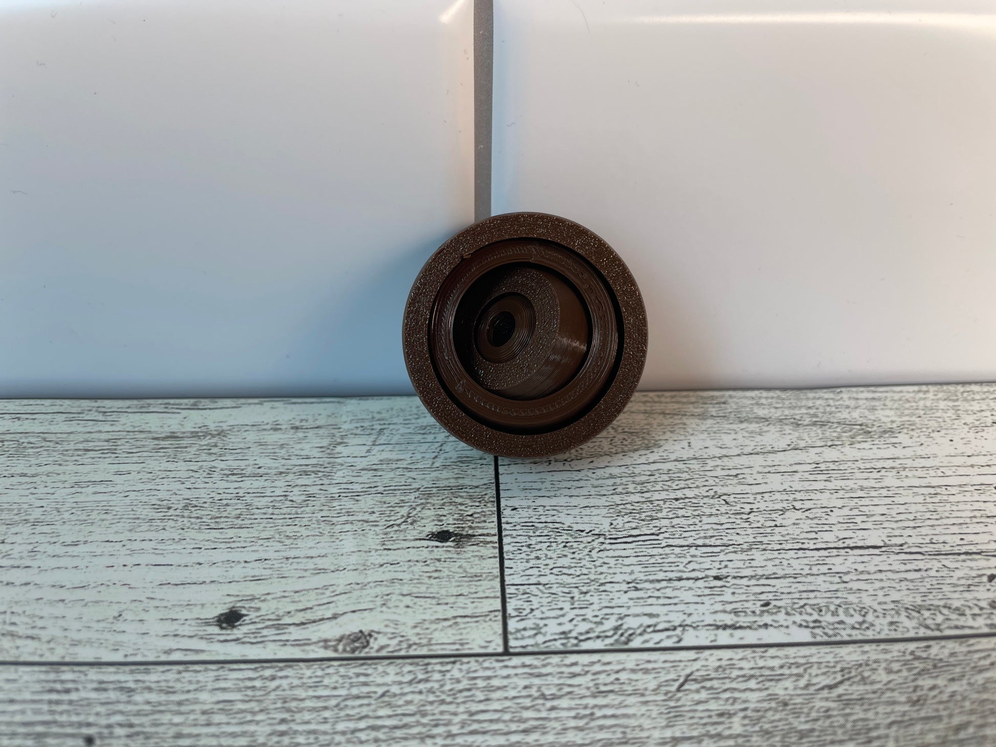 A brown gyro fidget without keychain on a light wood grain and white tile background.