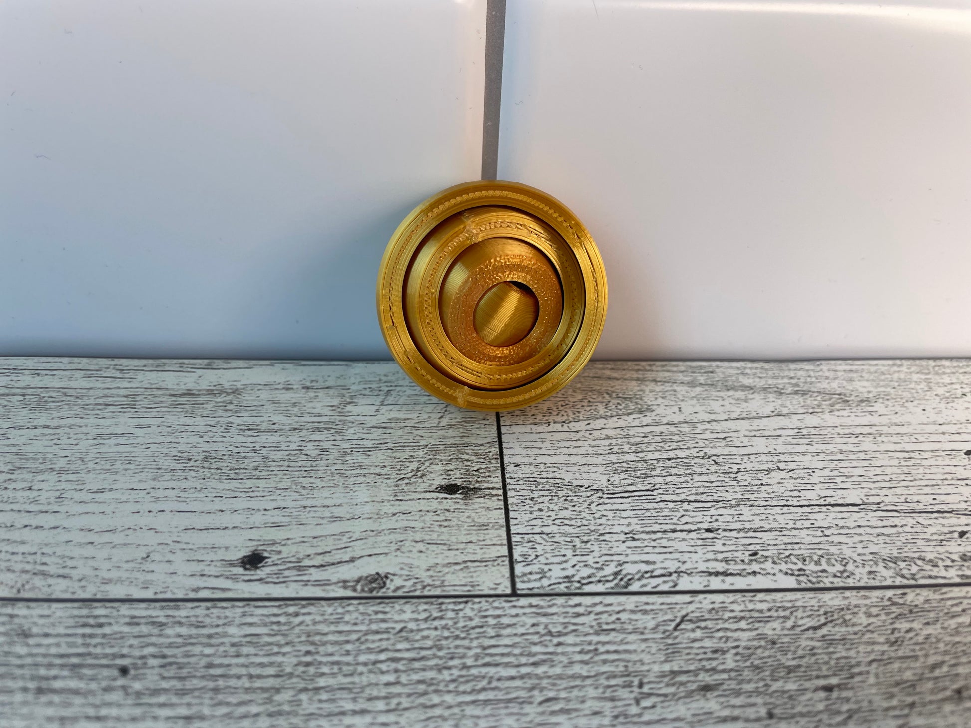 A gold gyro fidget without keychain on a light wood grain and white tile background.