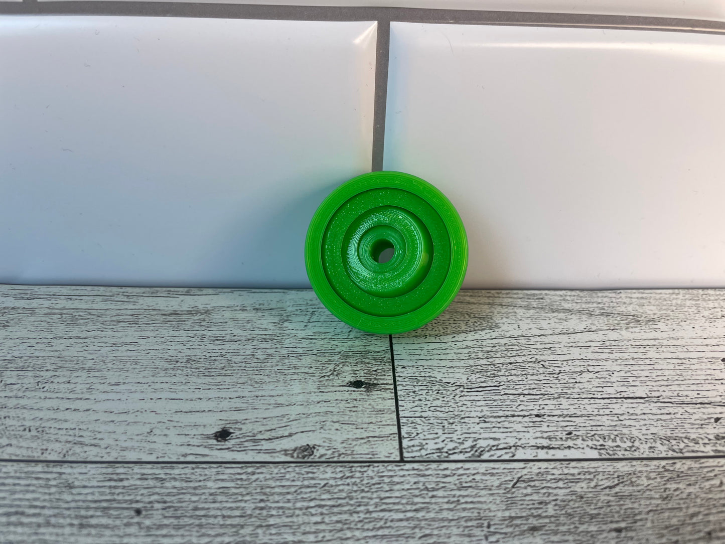 A lime green gyro fidget without keychain on a light wood grain and white tile background.