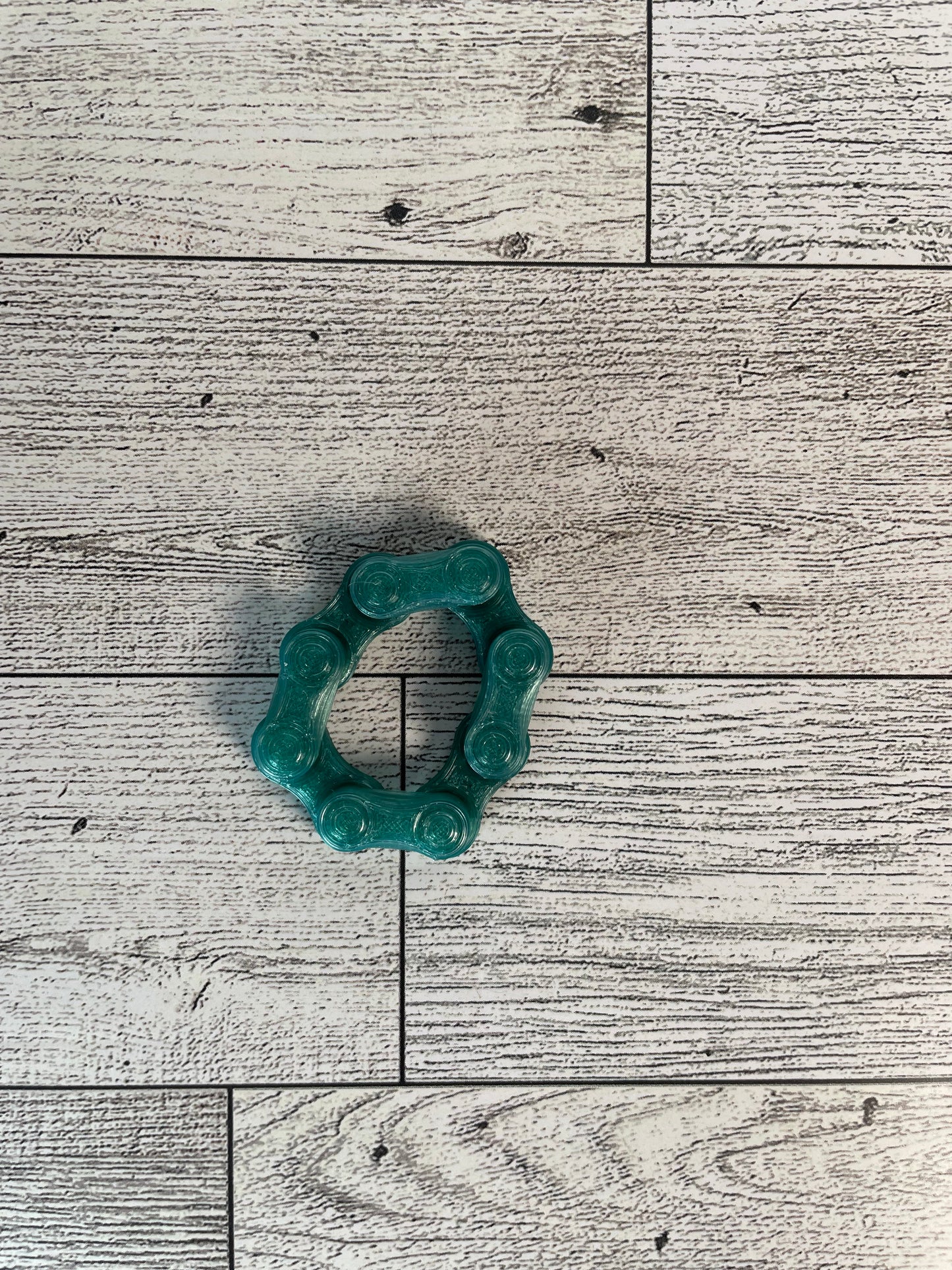 A translucent green chain link on a wood backdrop. The chain is arranged in a circle shape and there are four links