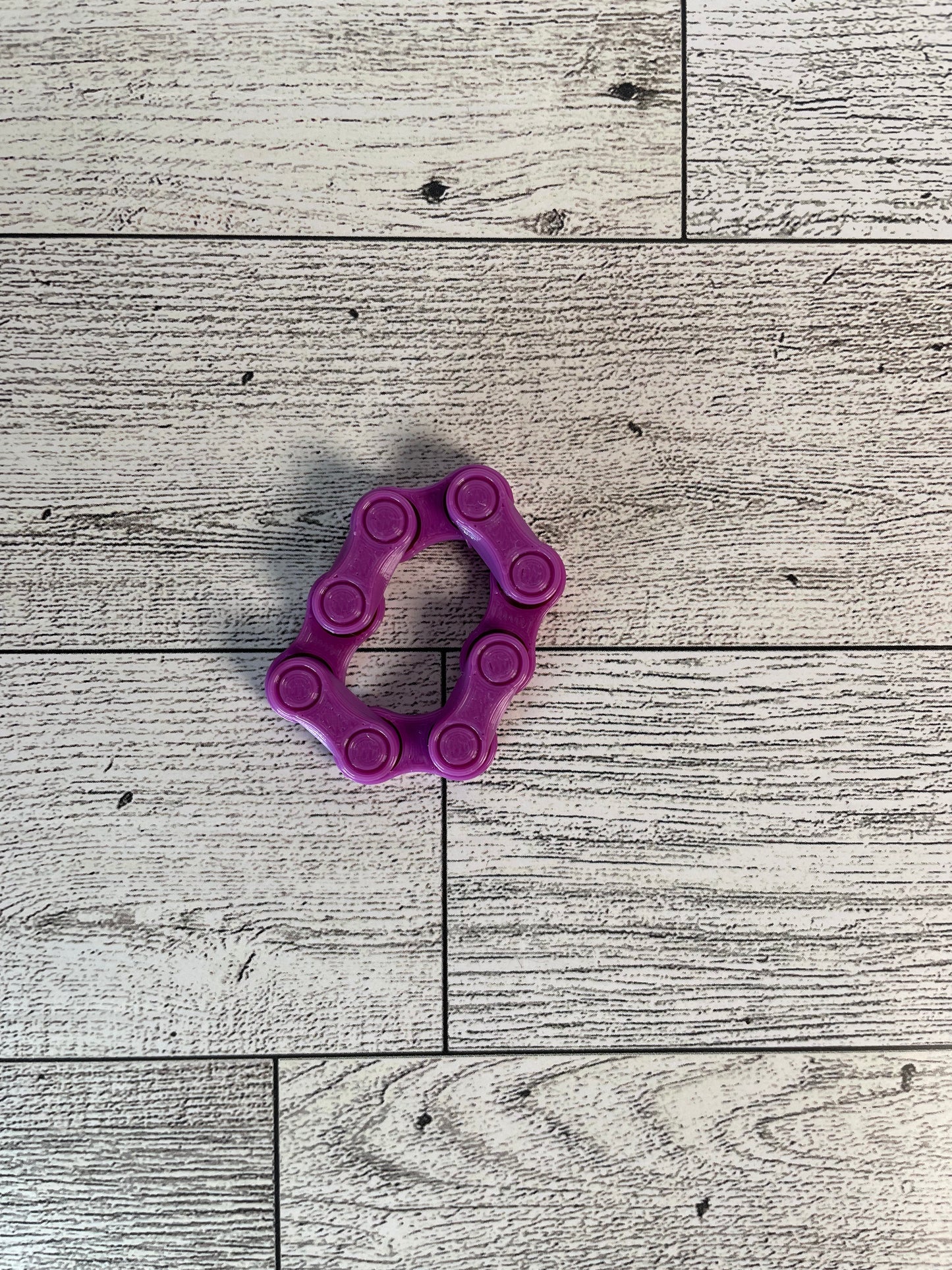 A purple chain link on a wood backdrop. The chain is arranged in a oval shape and there are four links.