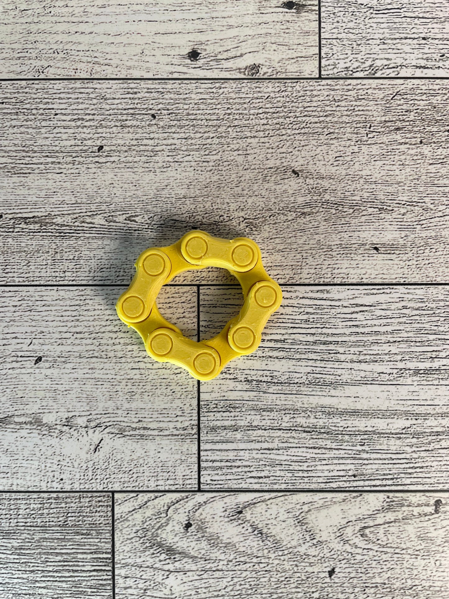 A yellow chain link on a wood backdrop. The chain is arranged in a circle shape and there are four links.