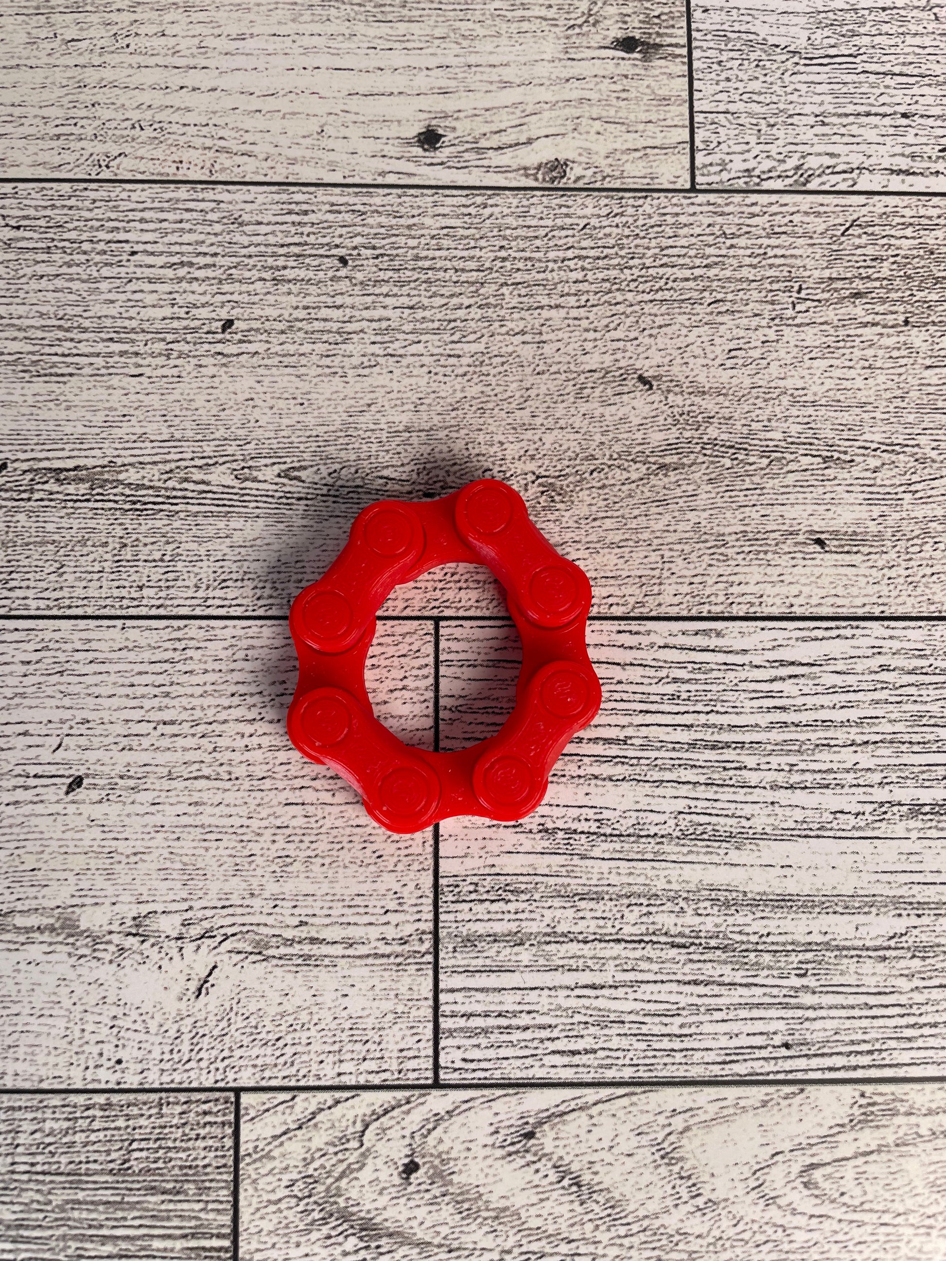 A red chain link on a wood backdrop. The chain is arranged in a circle shape and there are four links.