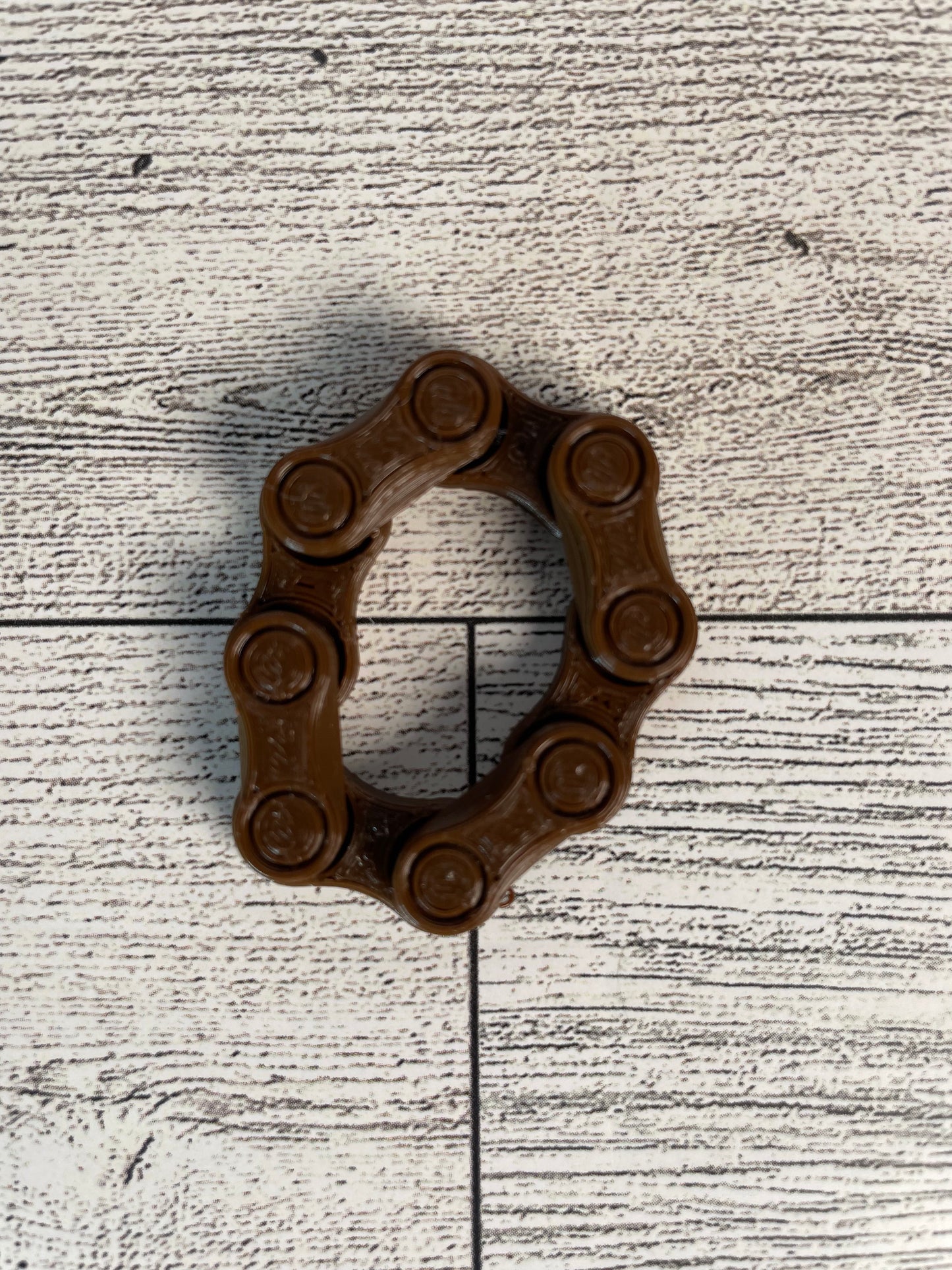 A brown chain link on a wood backdrop. The chain is arranged in a circle shape and there are four links