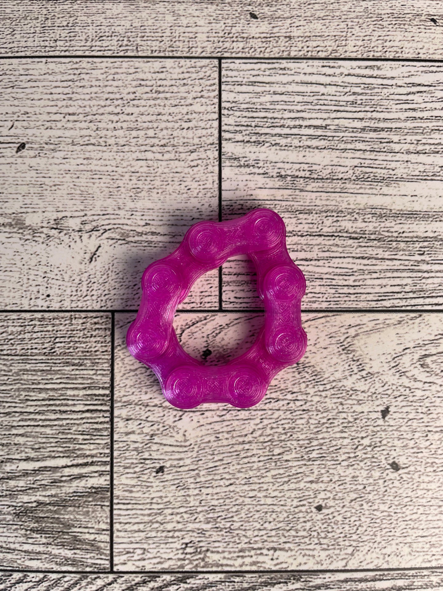A translucent purple chain link on a wood backdrop. The chain is arranged in a circle shape and there are four links