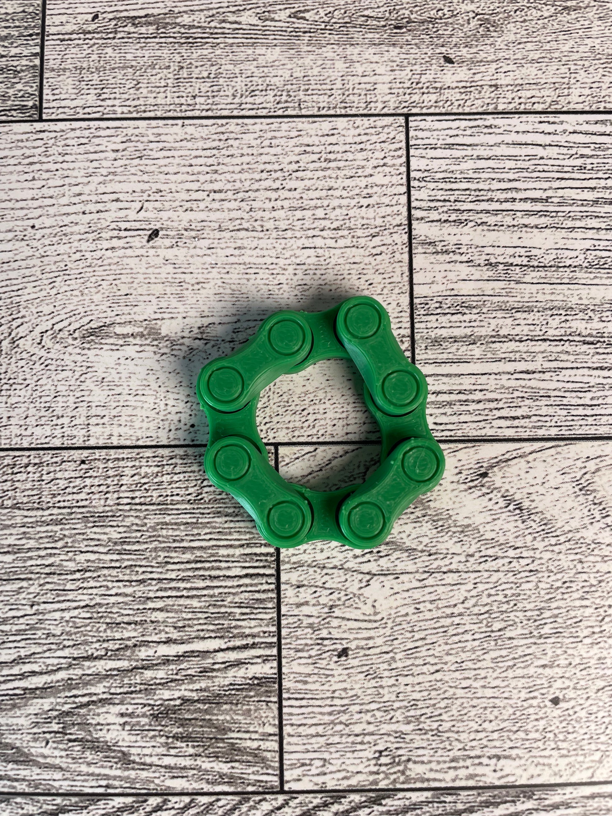 A green chain link on a wood backdrop. The chain is arranged in a circle shape and there are four links.
