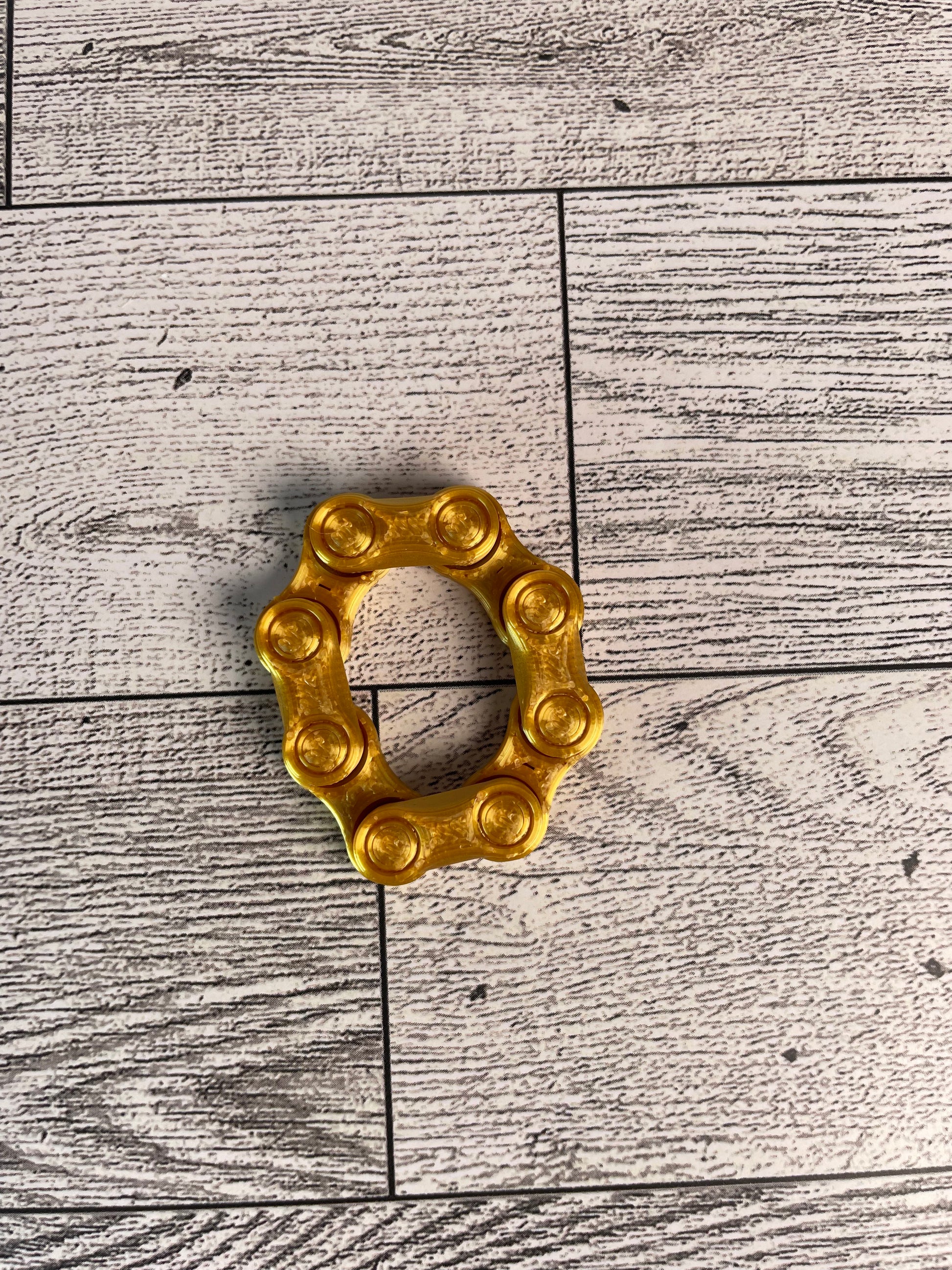 A gold chain link on a wood backdrop. The chain is arranged in a circle shape and there are four links