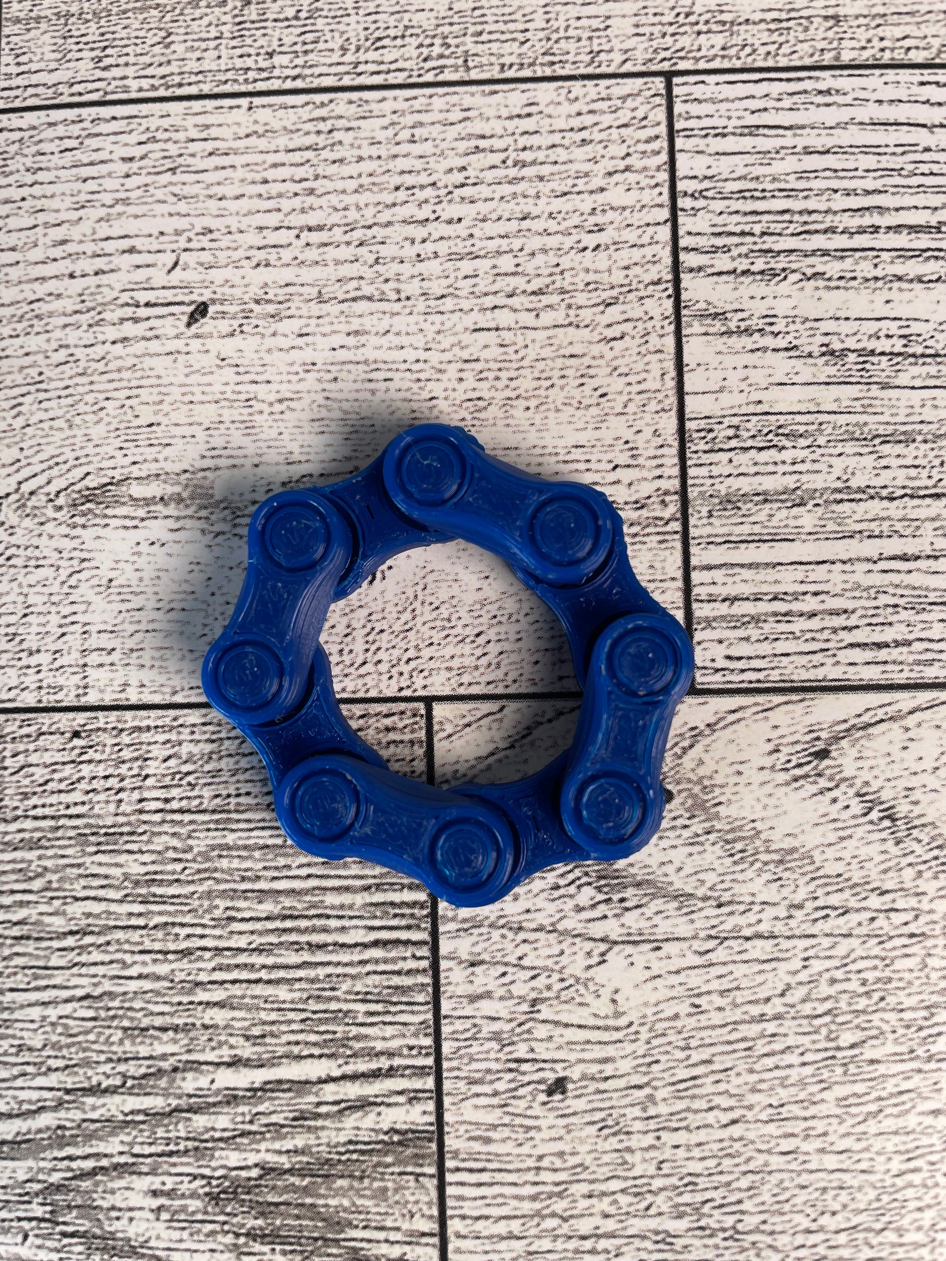 A blue chain link on a wood backdrop. The chain is arranged in a circle shape and there are four links.