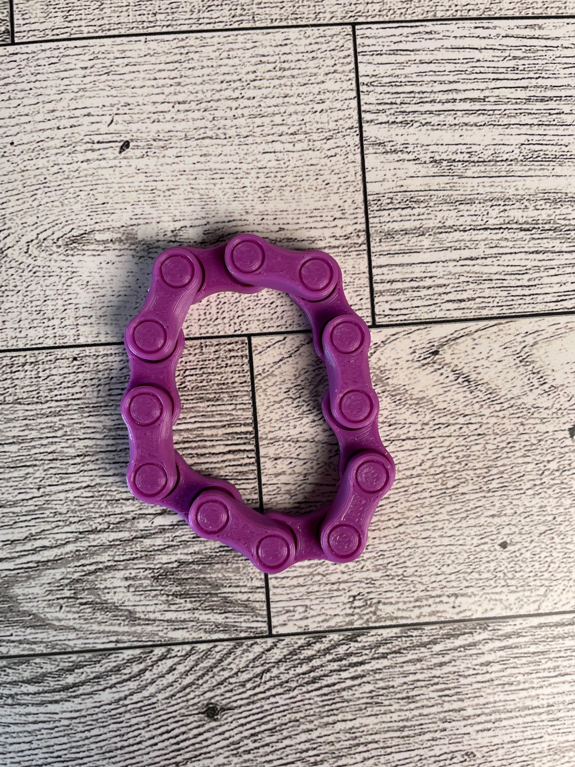 A purple chain link on a wood backdrop. The chain is arranged in a oval shape and there are six links.
