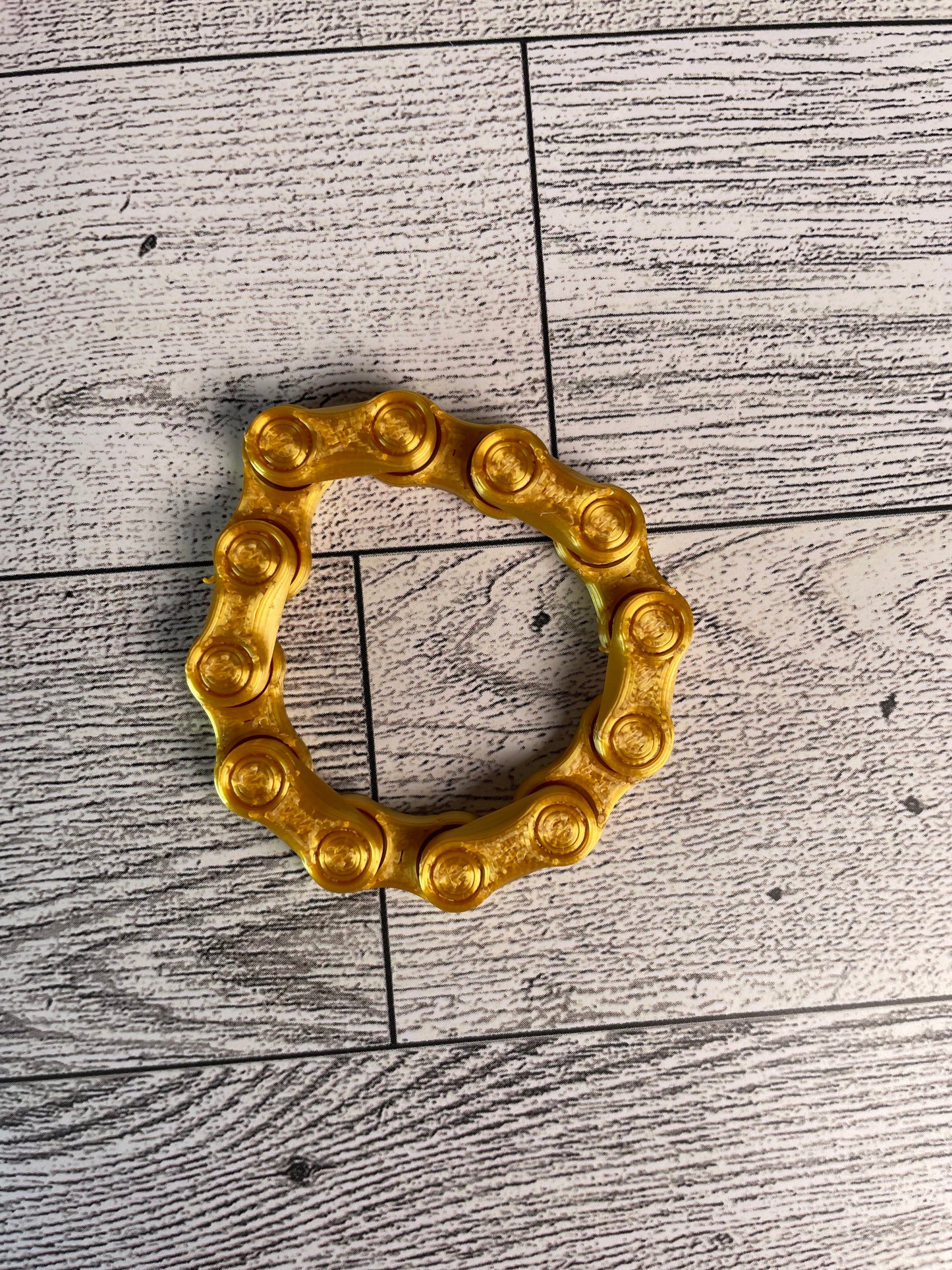 A gold chain link on a wood backdrop. The chain is arranged in a circle shape and there are six links.