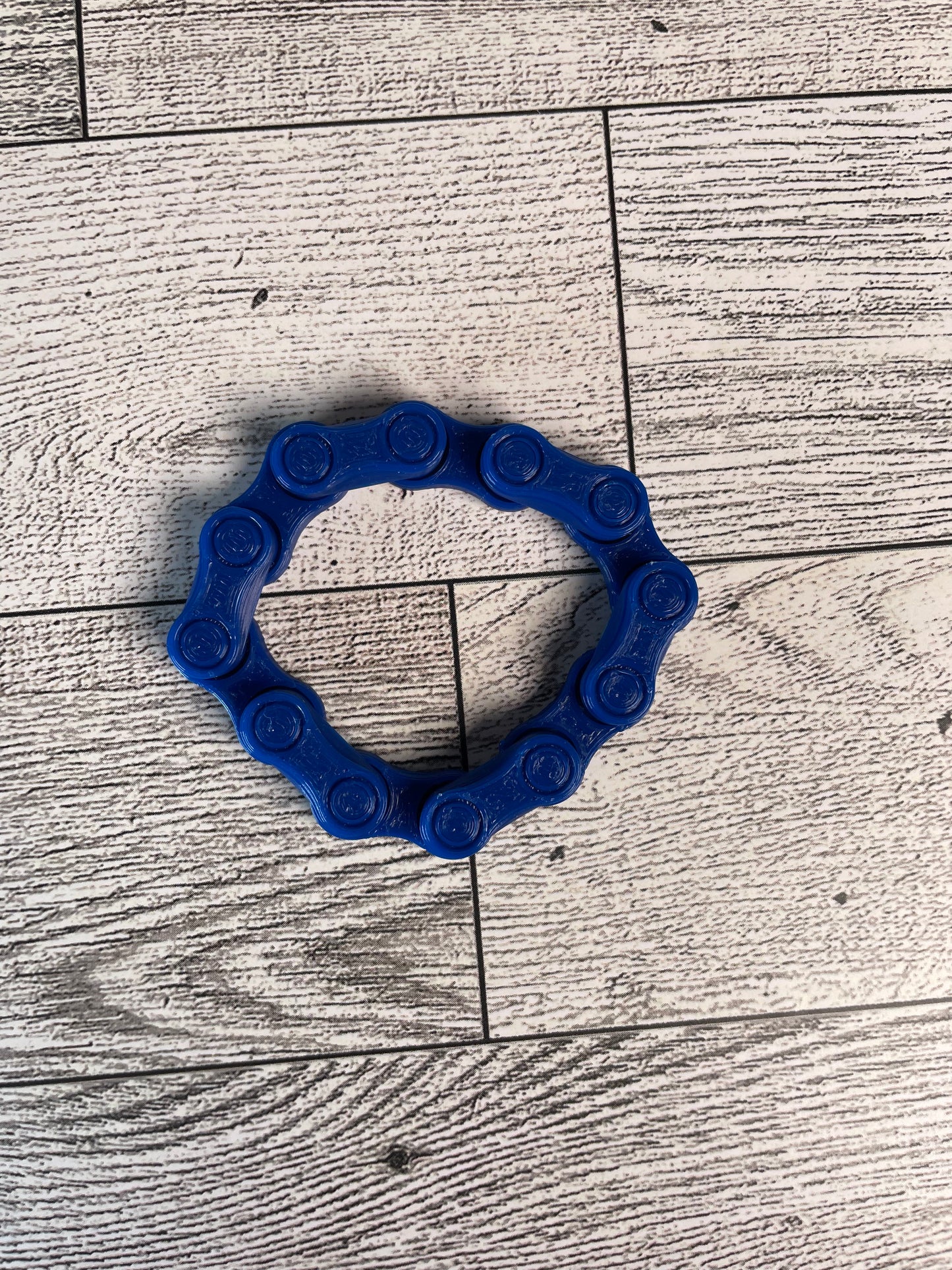 A blue chain link on a wood backdrop. The chain is arranged in a circle shape and there are six links.