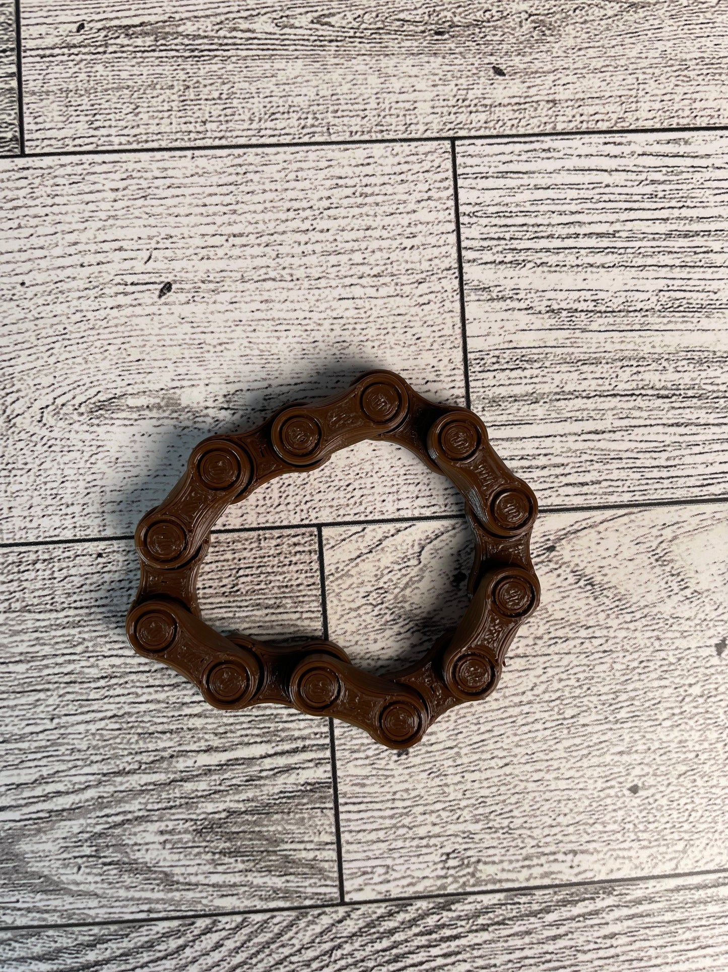 A brown chain link on a wood backdrop. The chain is arranged in a triangle shape and there are six links.