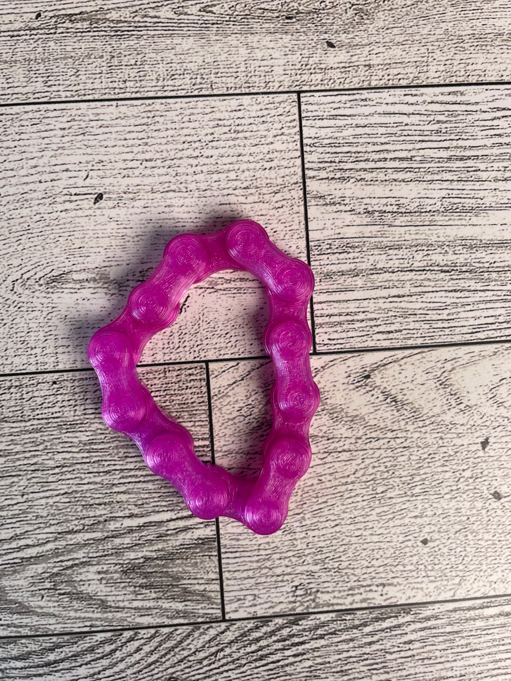 A translucent purple chain link on a wood backdrop. The chain is arranged in a triangle shape and there are six links.