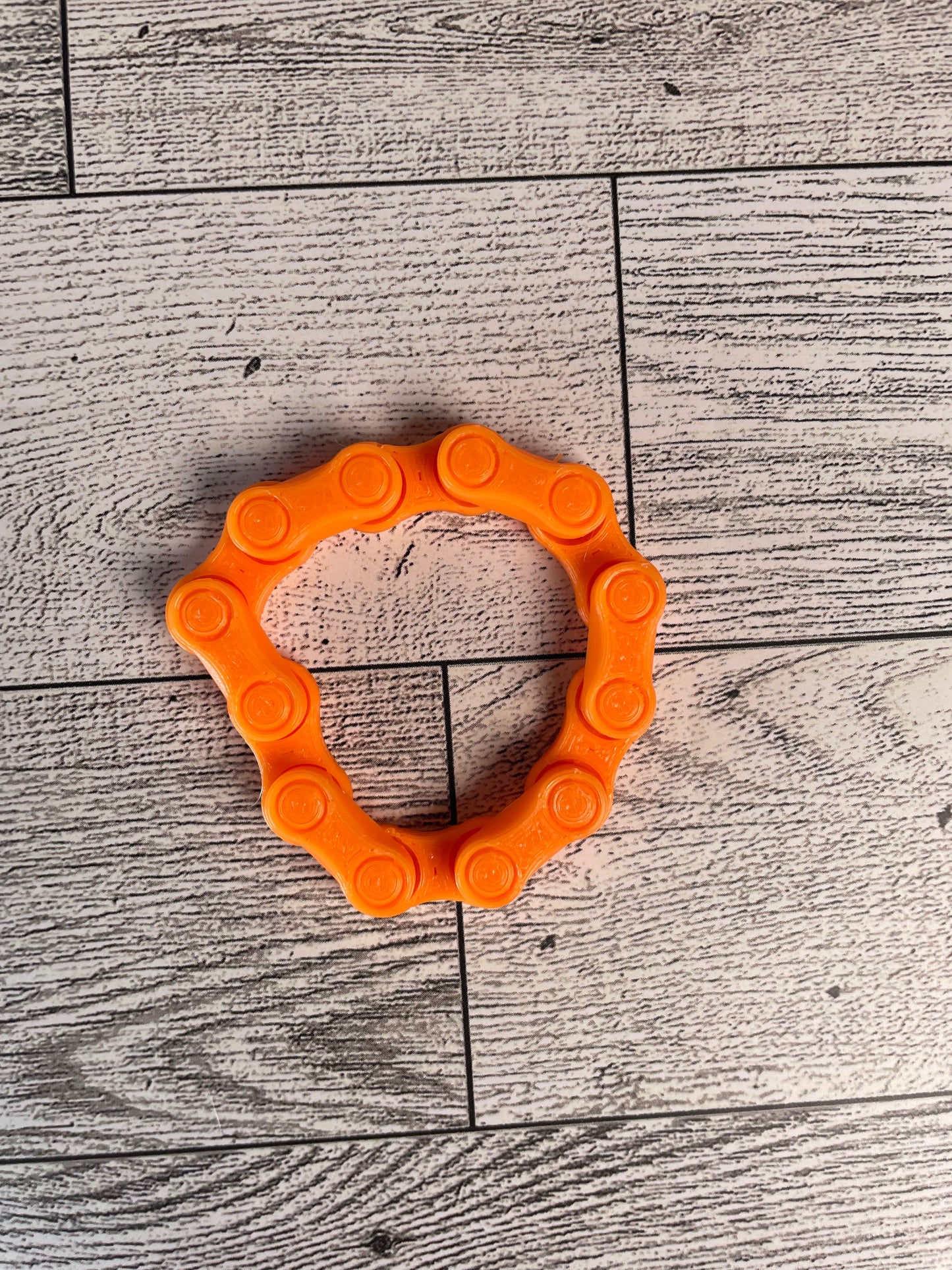 A orange chain link on a wood backdrop. The chain is arranged in a circle shape and there are six links.
