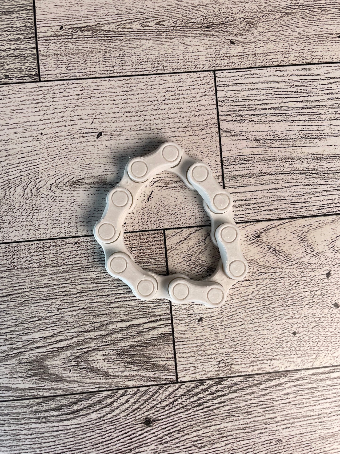 A white chain link on a wood backdrop. The chain is arranged in a circle shape and there are six links.