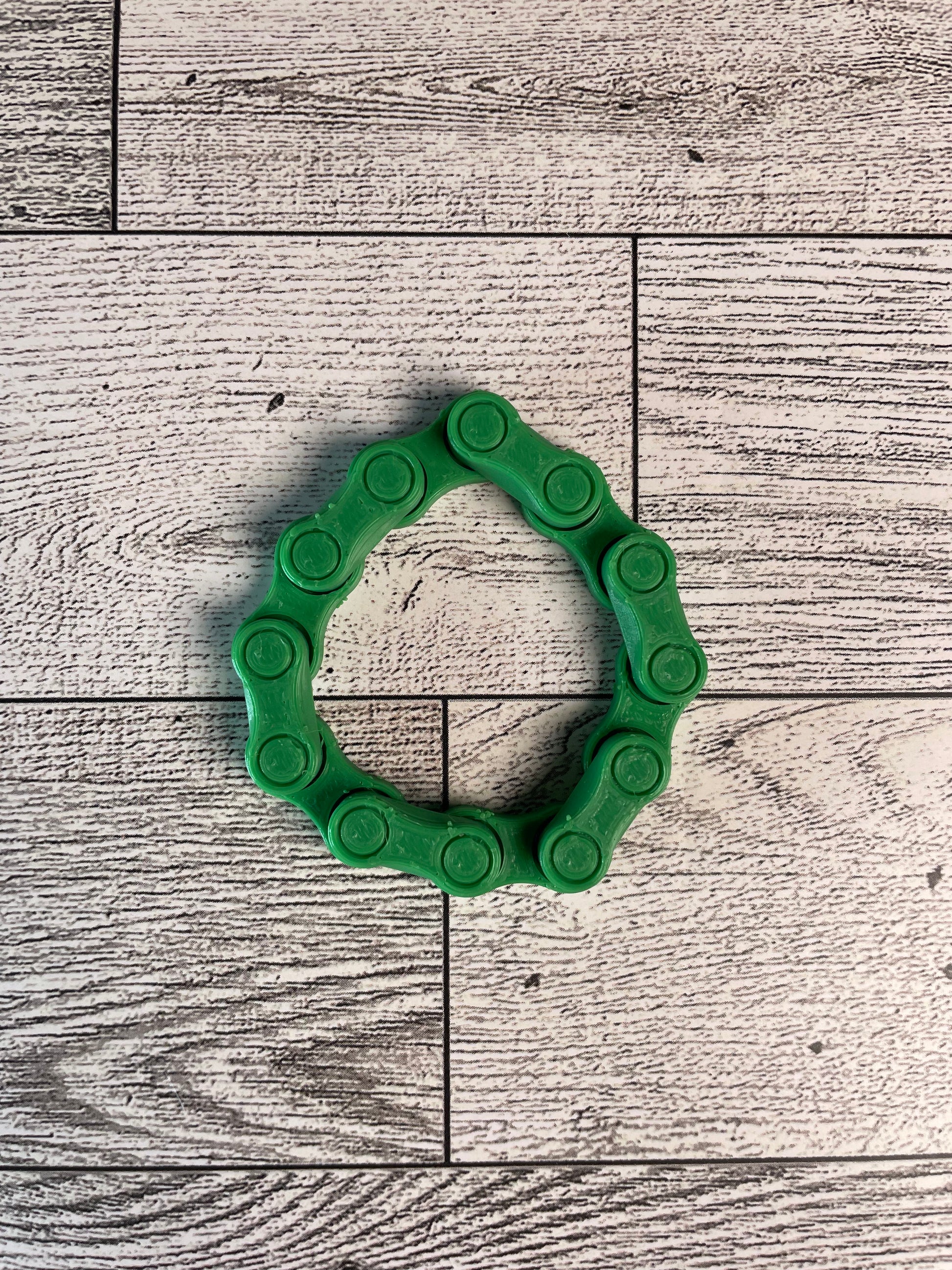 A green chain link on a wood backdrop. The chain is arranged in a circle shape and there are six links.