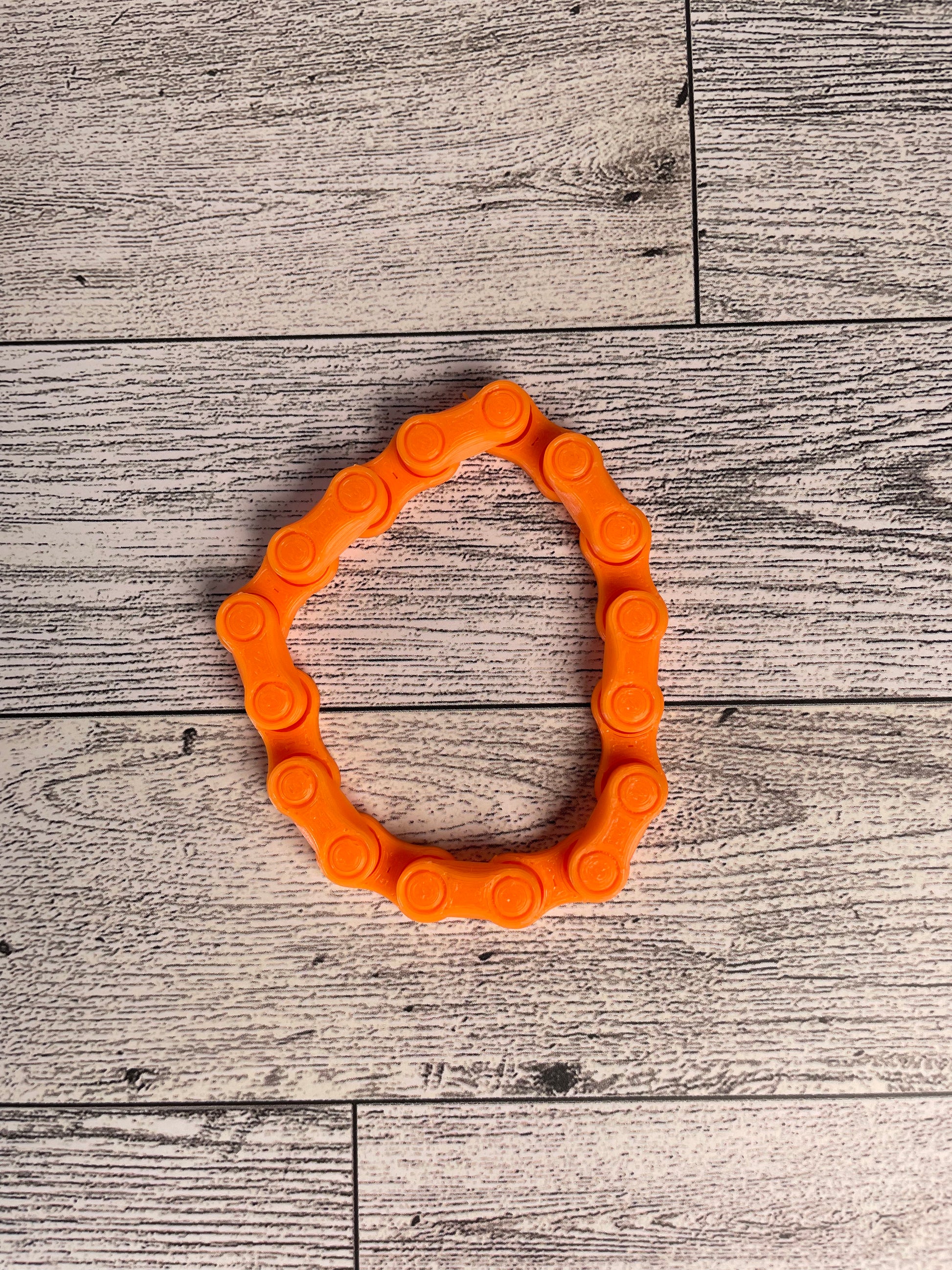 A orange chain link on a wood backdrop. The chain is arranged in a circle shape and there are eight links.