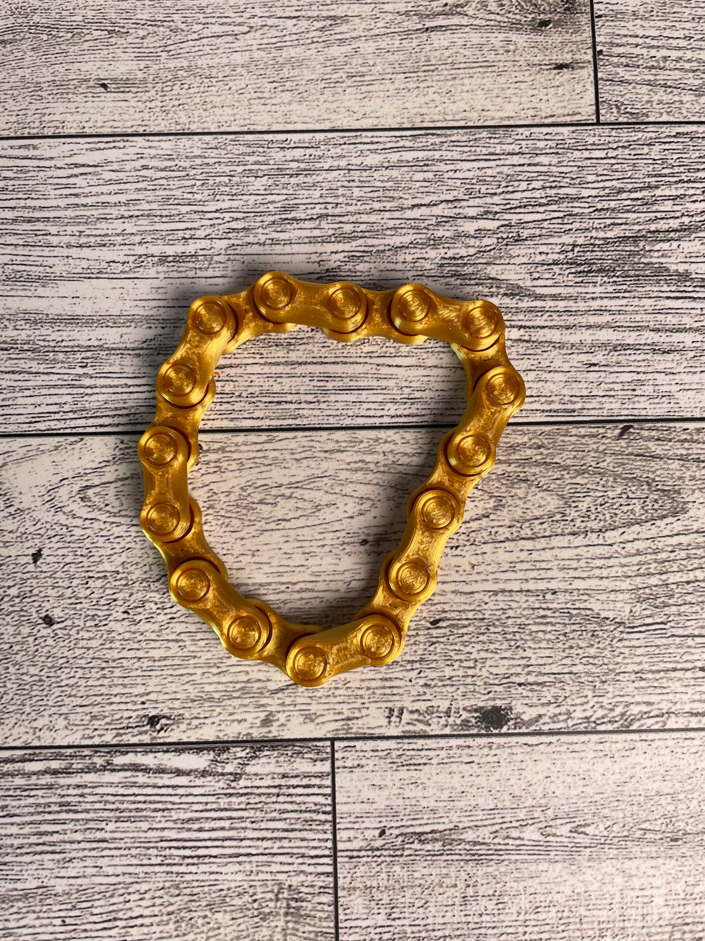 A gold chain link on a wood backdrop. The chain is arranged in a circle shape and there are eight links.