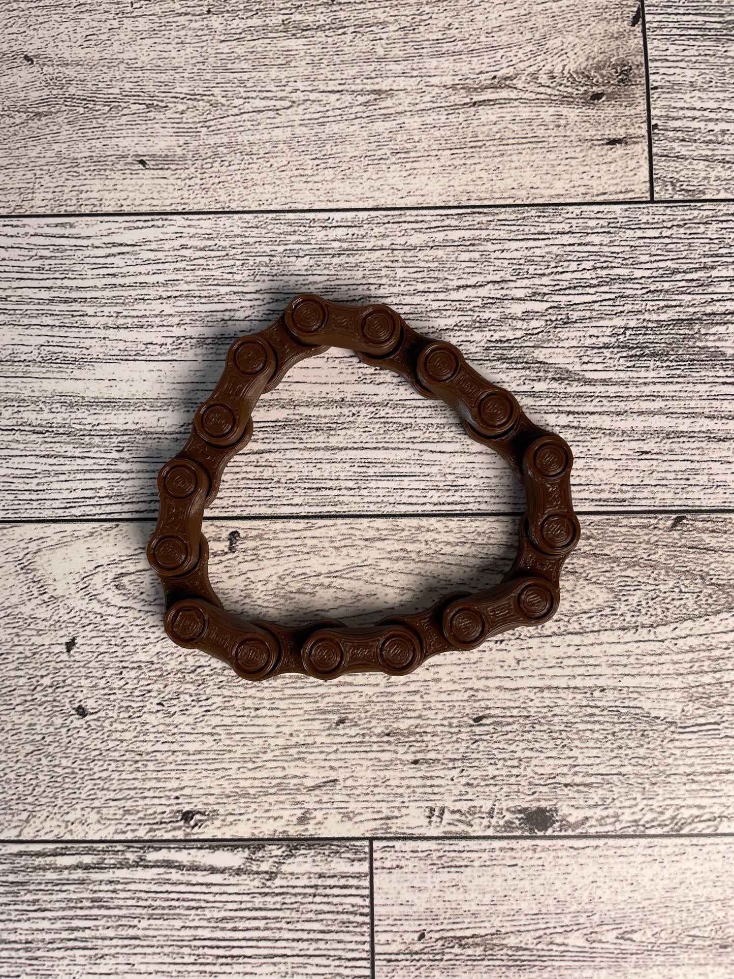 A brown chain link on a wood backdrop. The chain is arranged in a circle shape and there are eight links.