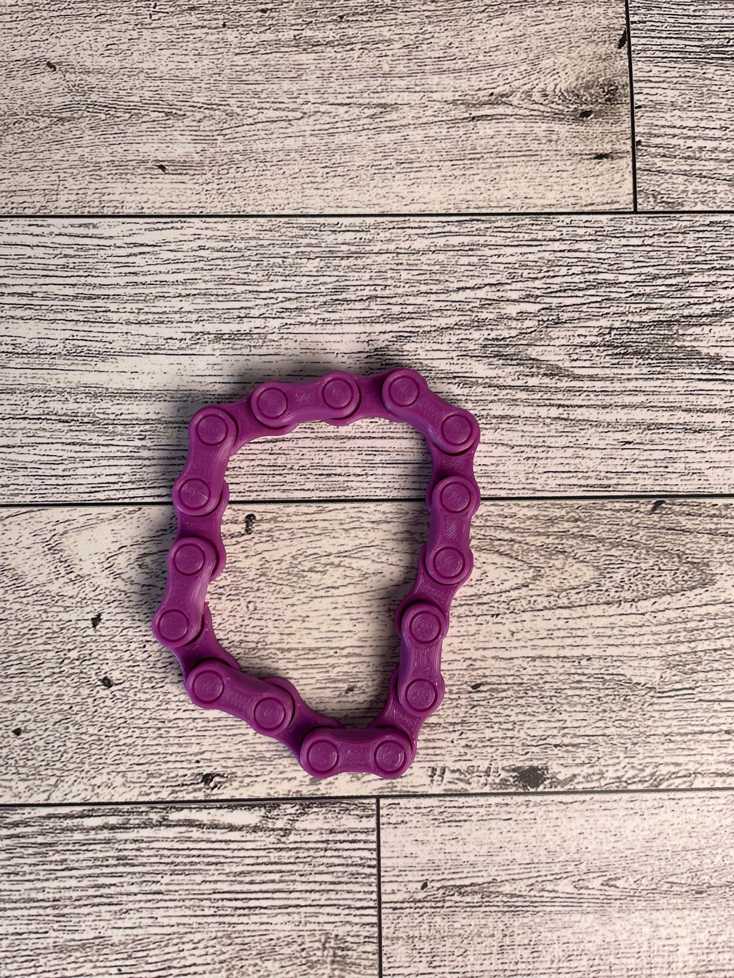 A purple chain link on a wood backdrop. The chain is arranged in a circle shape and there are eight links.